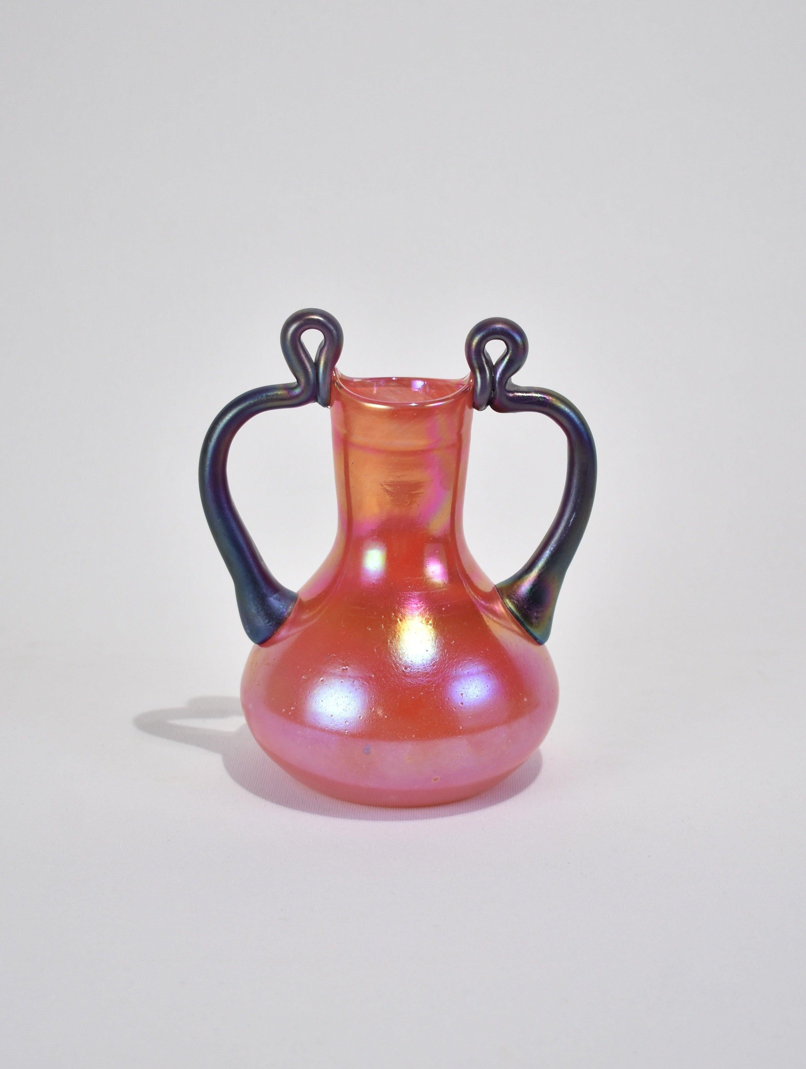 Beautiful, hand blown iridescent vase in red with two purple handles. Beautiful on its own or with a small arrangement of flowers. Signed on base.