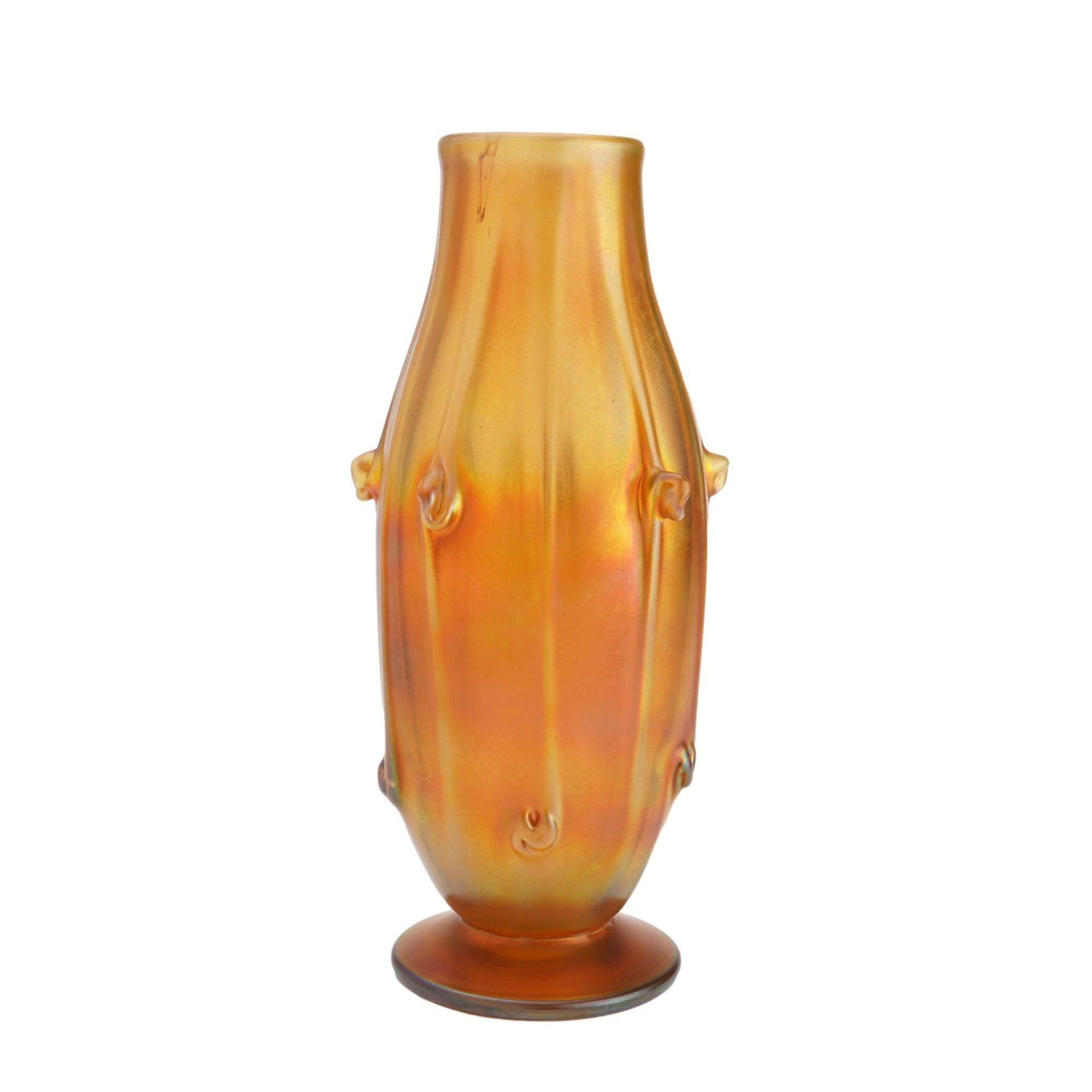 A distinctive elongated barrel form footed Favrile glass vase in iridescent gold. The surface of the vase is distinguished with elongated ribs with tight swirls alternating from the shoulder to the the bottom of the barrel which comes to a waisted