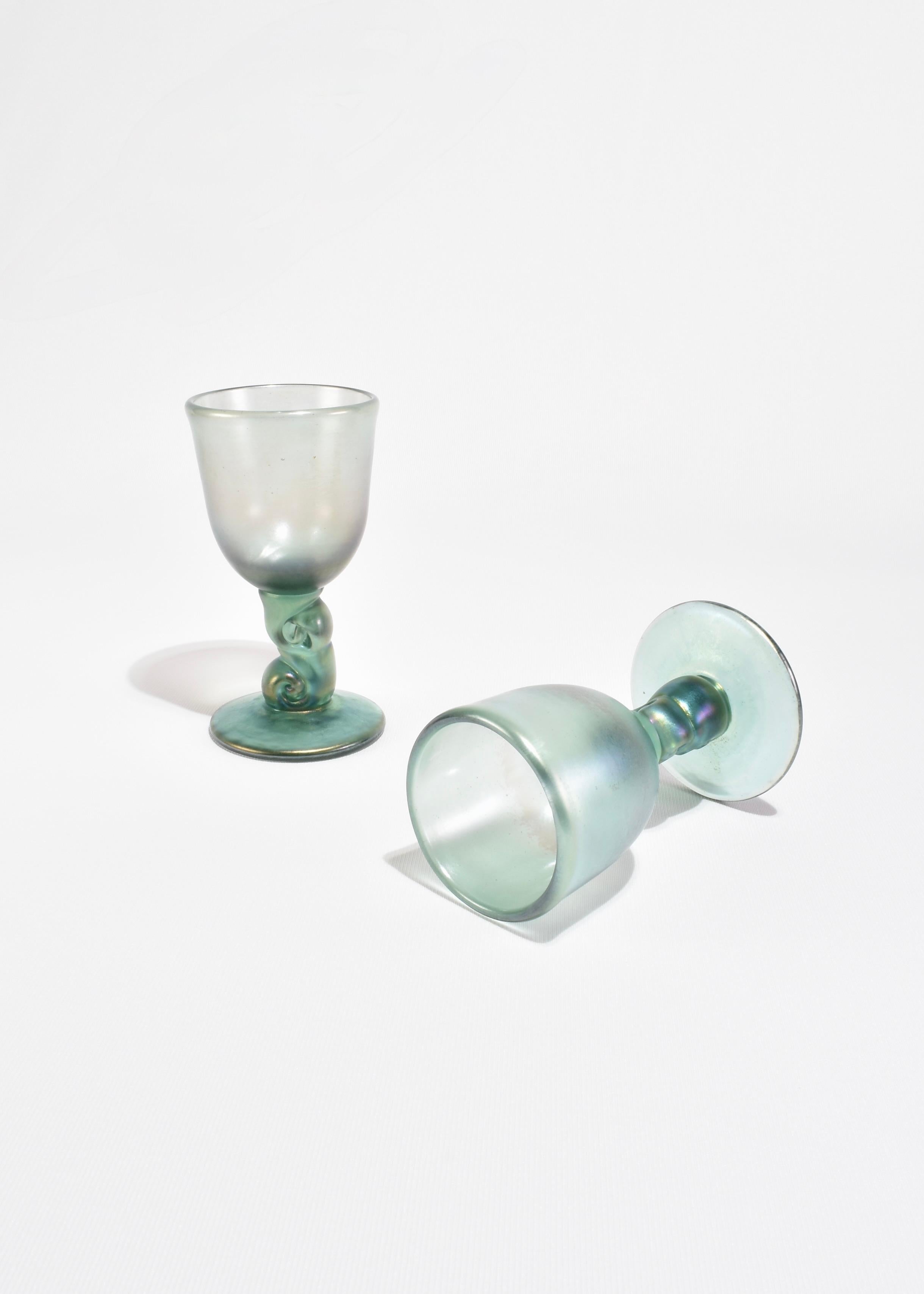 Calici iridescenti soffiati a mano di colore verde mare con coppe satinate e steli scultorei attorcigliati. Ogni bicchiere cattura la luce con note di viola, blu e oro. Venduti in coppia, firmati sulla base.