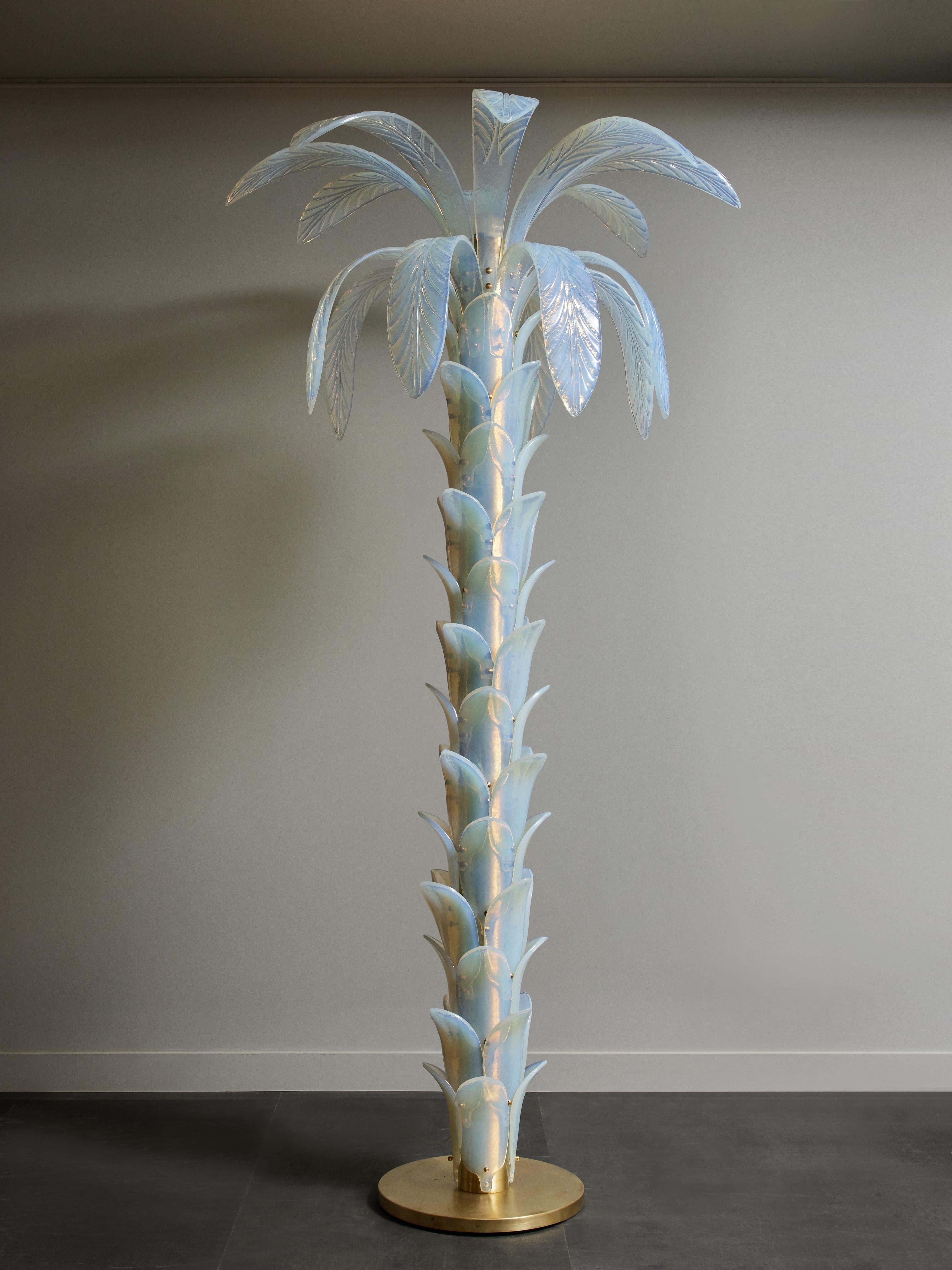 Tall floor lamp shaped like a palm tree, made of a brass circular base and trunk, covered with iridescent Murano glass leaves up to the top where large leaves burst out of the trunk.
One source of light at the top.
 