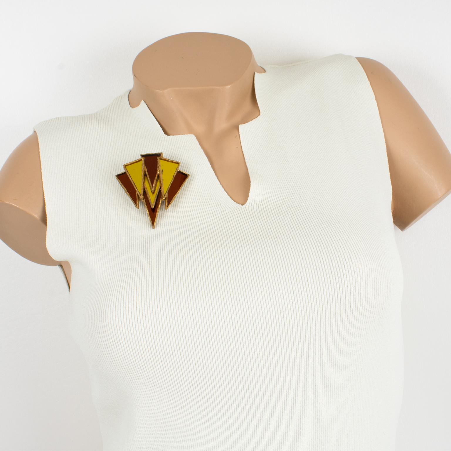 It is a striking Talosel or resin pin brooch designed by Irena Jaworska in the 1970s. 
The piece features a dimensional geometric modernist shape in gilded resin framing, topped with triangle mirrors in yellow and burnt orange colors. The pin is