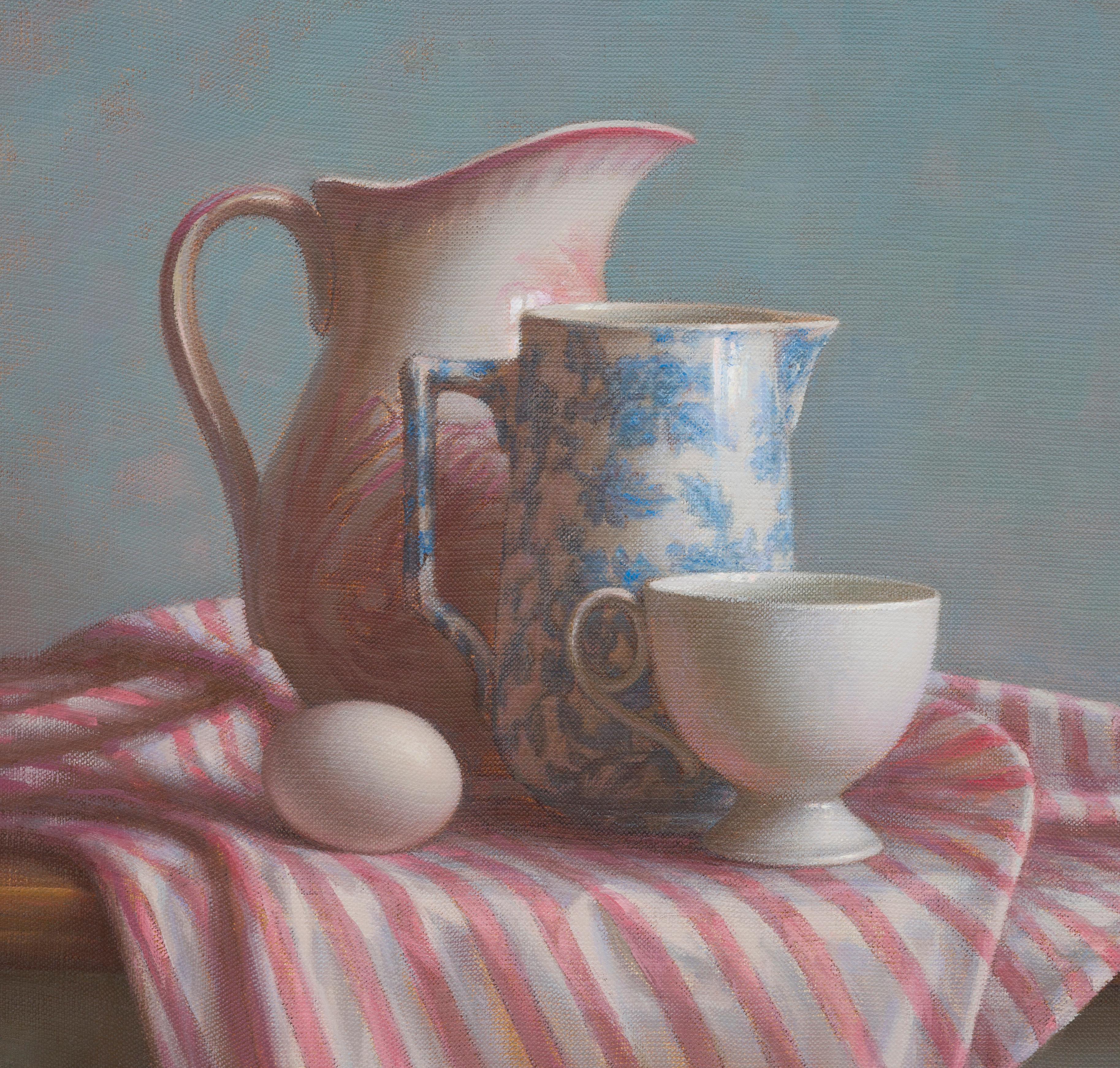  Une nature morte à l'huile lumineuse, où la lumière glisse sur une table drapée, révélant l'éclat tendre de la porcelaine et le jeu des plis soyeux. Deux cruches blanches, une tasse et un œuf forment un seul groupe sculptural au centre de la scène.