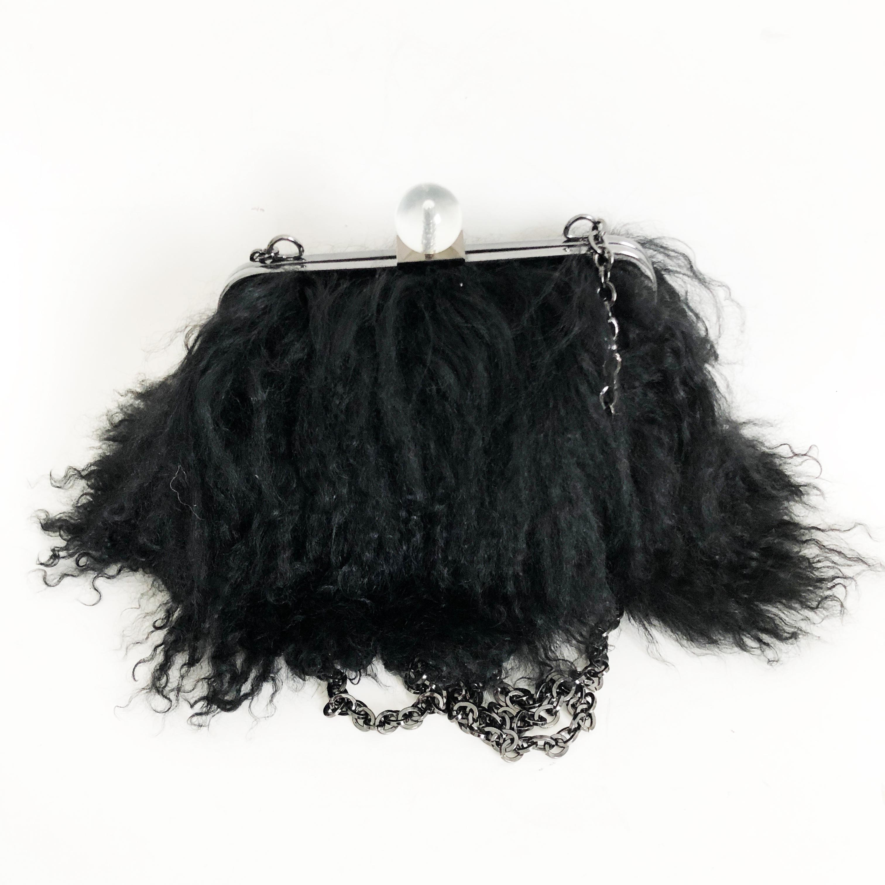 Iris Apfel Extinctions Black Mongolian Lamb Fur Bag. Features a chain strap for shoulder wear or can be stowed in the bag for use as a clutch. Lined in blue grosgrain fabric. Fastens with clear bubble clasp. Preowned with minimal signs of prior