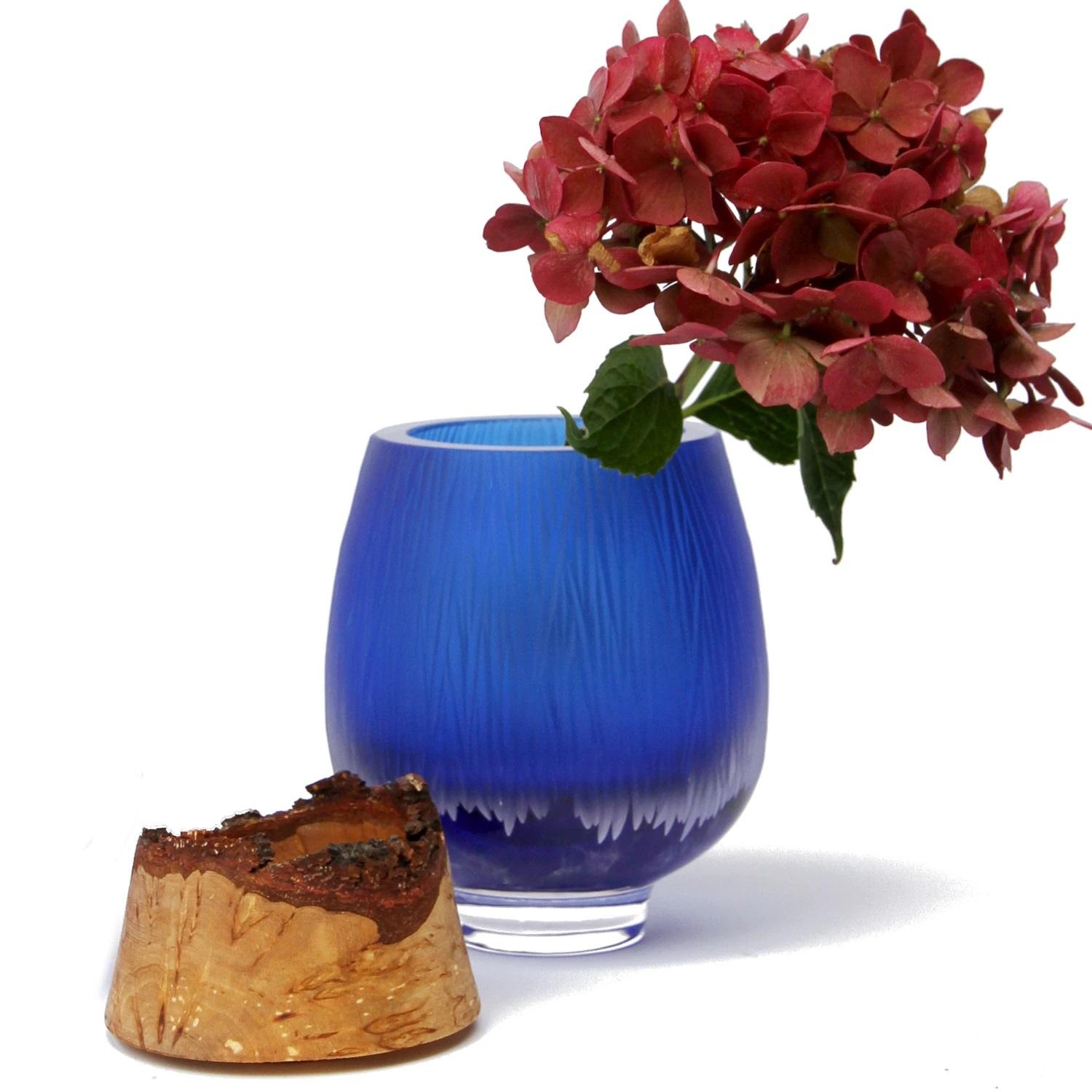 Iris Blue Frida with fine cuts stacking vessel, Pia Wüstenberg
Dimensions: D 13 x H 20
Materials: cut glass, wood
Available in other colors.

With its sculpted glass topped by Curly Birch, Poppy is an exquisite vessel. This delightful piece