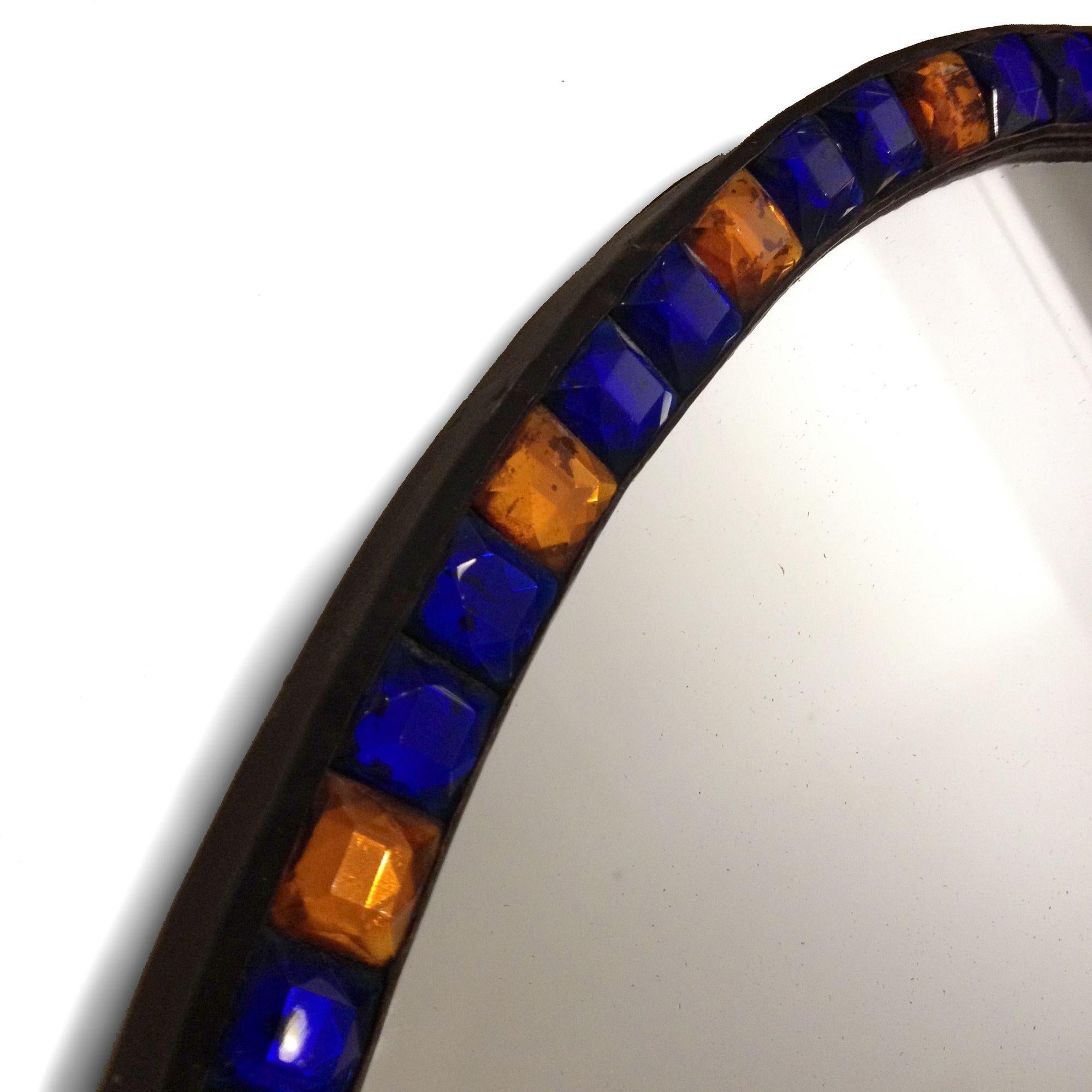 The alternating blue and amber faceted glass gems set into a metal oval frame.

