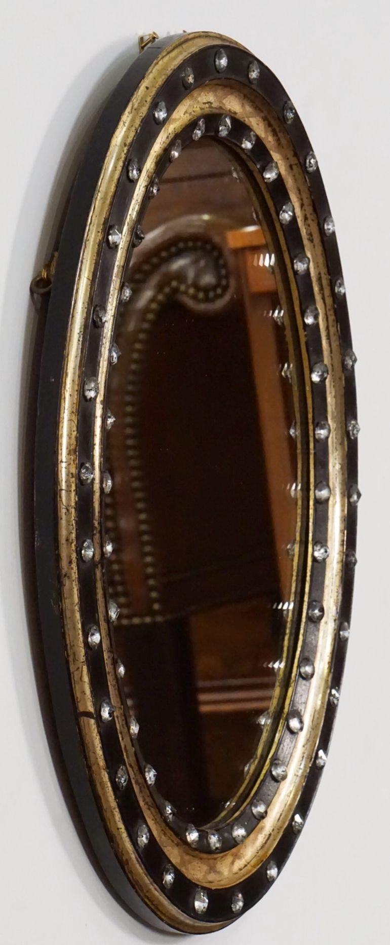 A fine Irish oval wall mirror from the 19th century, featuring a distinctive frame of alternating raised ebonized slips with original faceted glass stud decorations (Waterford border beads), separated by gilded and X-decorated recesses. 

Measures: