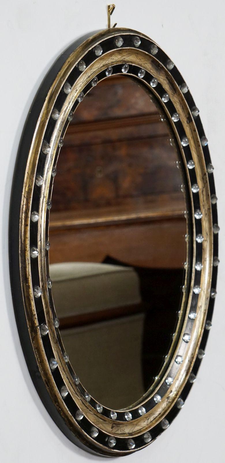A fine Irish oval wall mirror from the 19th century, featuring a distinctive frame of alternating raised ebonized slips with original faceted glass stud decorations (Waterford border beads), separated by gilded and X-decorated recesses.

Measures: H