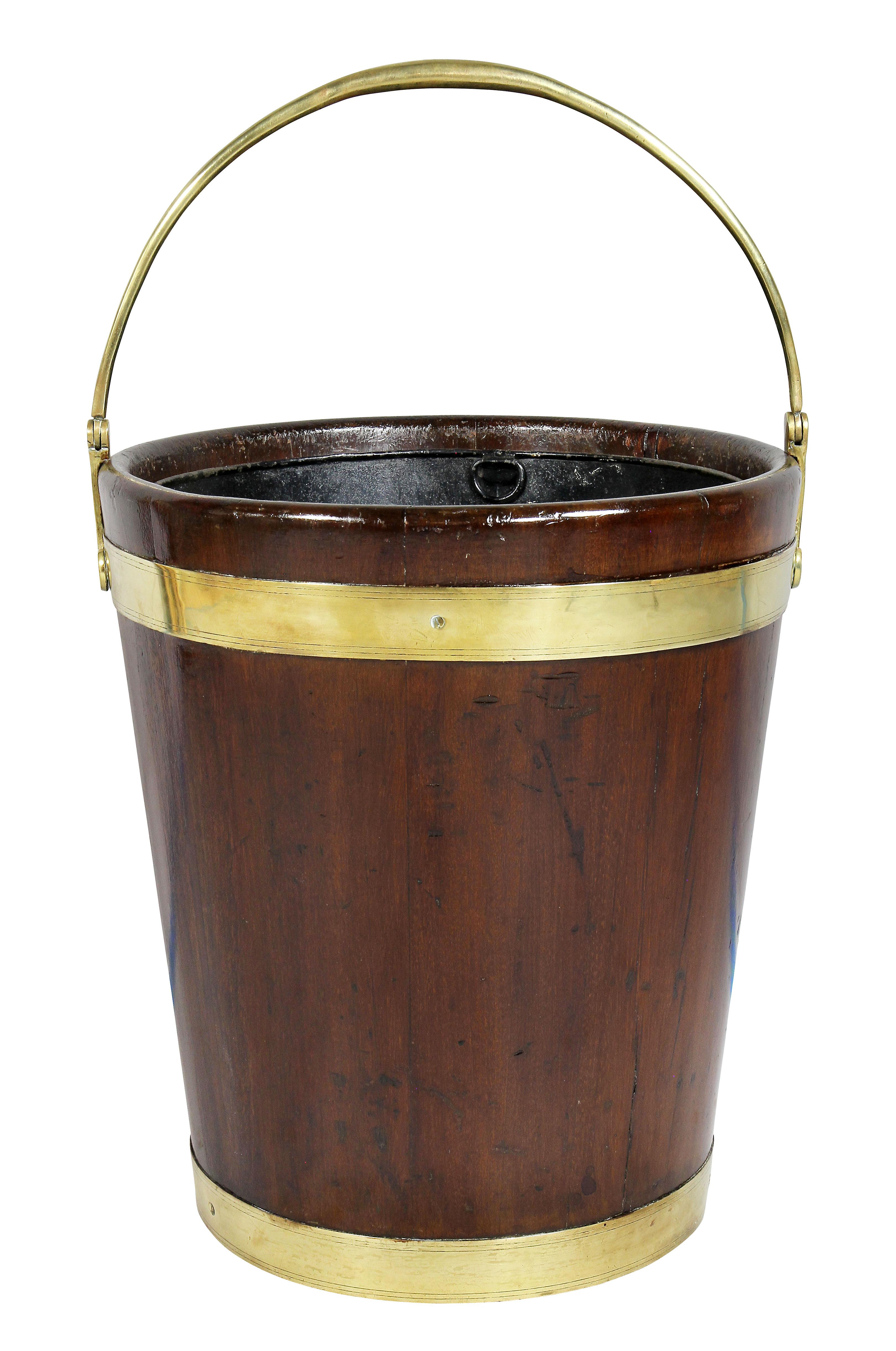 With brass loop handle, tin liner and tapered cylindrical body with brass strapping.