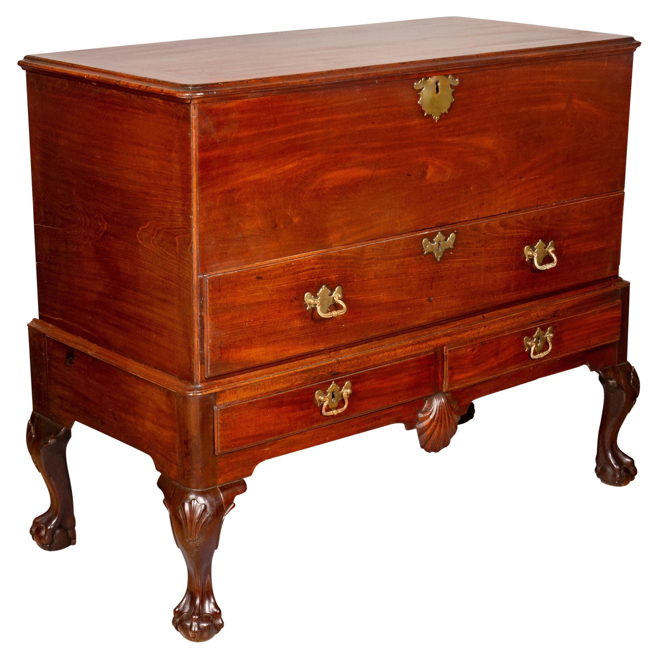 With a rectangular hinged top with molded edge over a conforming case with deep well over a long drawer. The base with two drawers over a central carved scallop shell , raised on cabriole legs with shell knees and ball and claw feet. With brass