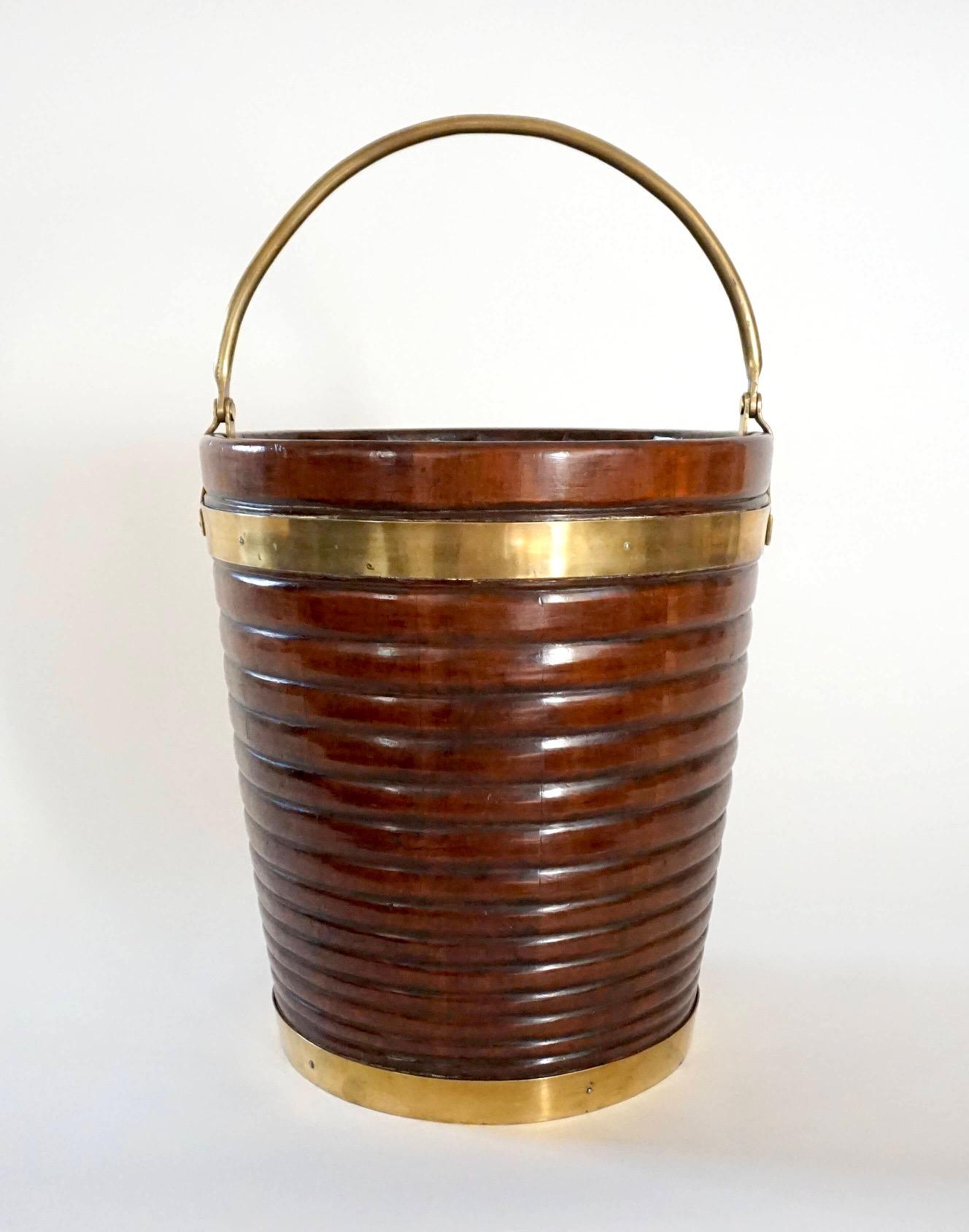 An exceptional Irish George III period mahogany and brass bound peat bucket of good size and unusual design with uniquely hinged brass swing handle; the body of tapered stave-construction with graduated ring-turned carving. Height given with handle