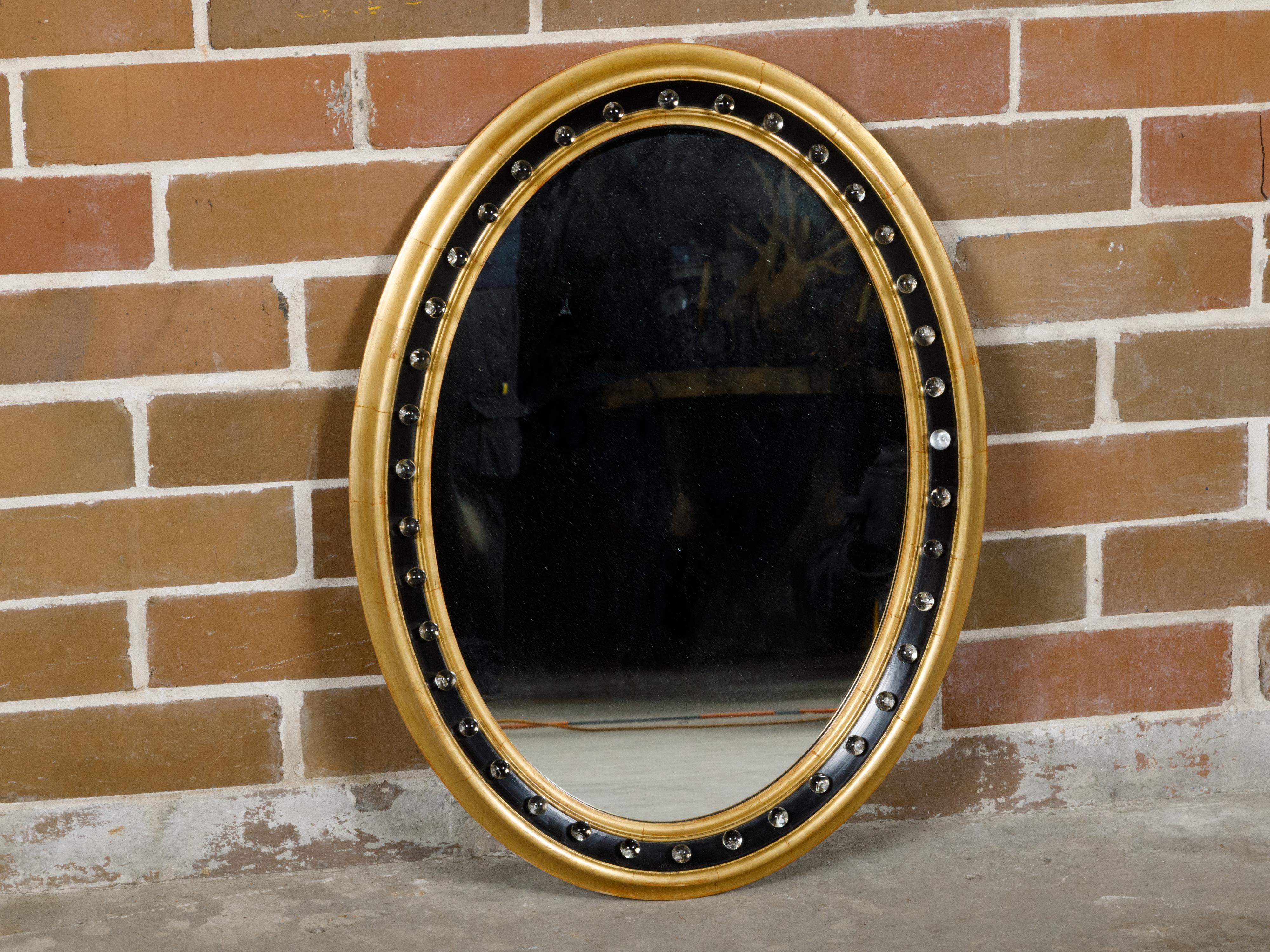 An Irish black and gold oval shaped wall mirror from circa 1920 with petite glass spheres. Experience the enchanting blend of elegance and uniqueness with this Irish black and gold oval-shaped wall mirror from circa 1920. This mirror, with its