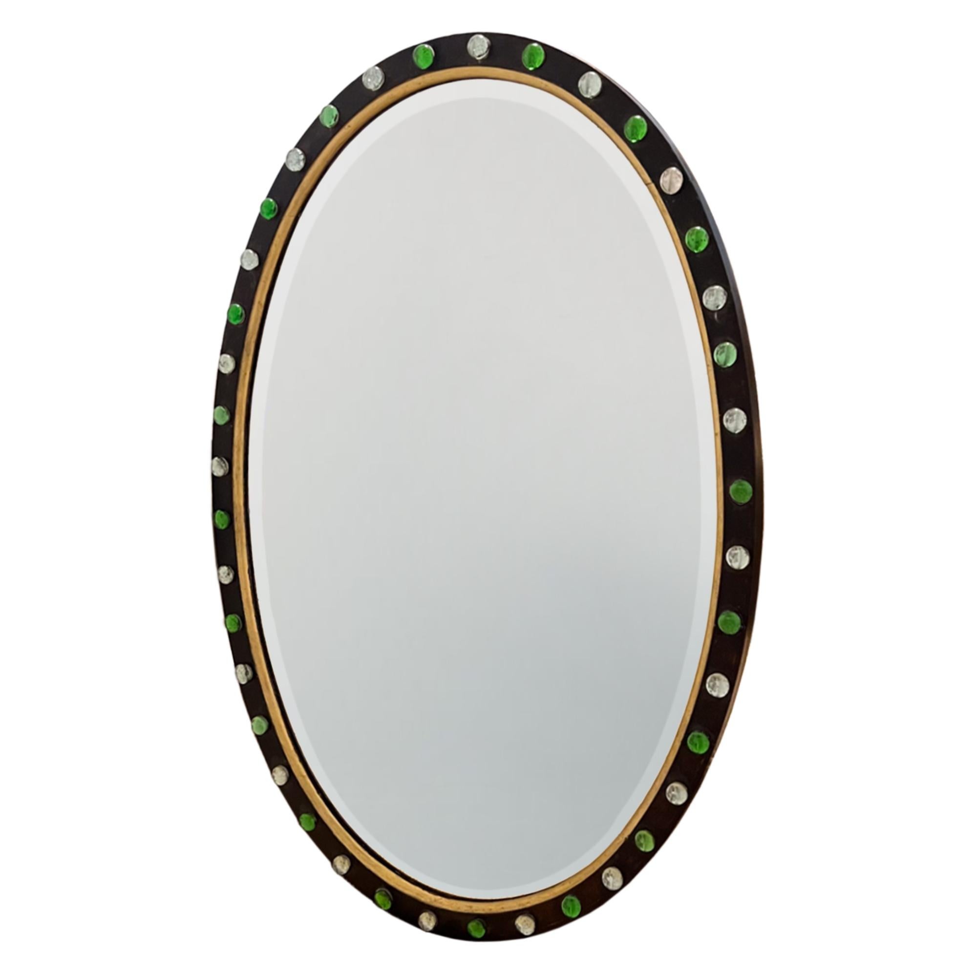 This is a beautiful, decorative oval mirror. Made in Ireland in the early 20th century. 

It has alternate emerald and clear glass cabochons around the edge - all are intact. The original plate has some foxing consistent with it's age.

Lovely