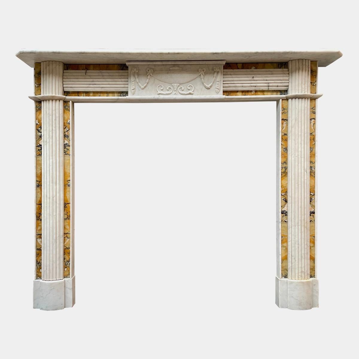 An Irish antique fireplace from the Regency period in Italian Carrara and Siena marbles. The jambs with demi lune reeded panels on book matched Sienna ingrounds, surmounted by conforming endblocks. The frieze with a carved centre tablet of urn and
