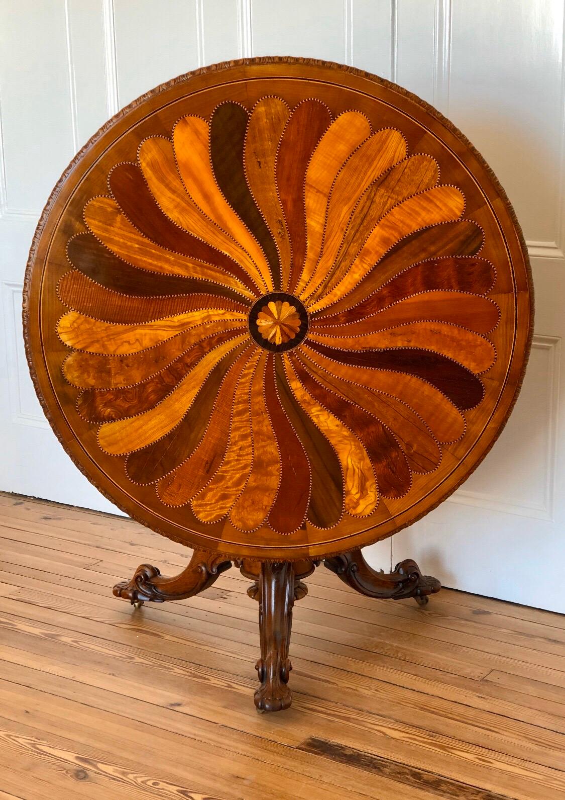 This British Colonial center table uses exotic wood veneers to create a spectacular spiral, fanning clockwise with contrasting exotic specimen woods extending from a central rosette fan compassed by an ebony band. The exotic spiral marquetry inlay