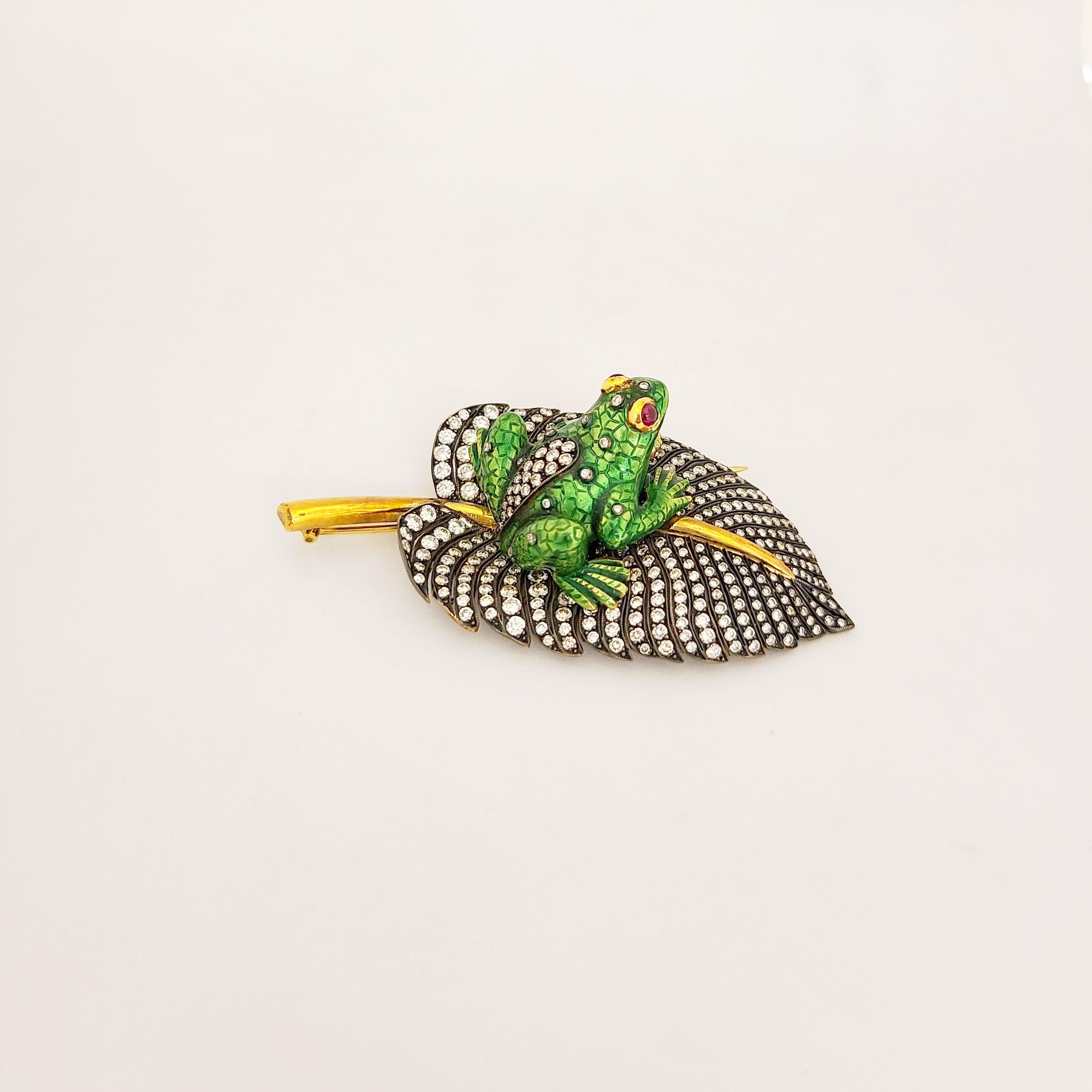 This exquisite brooch is crafted in 18 karat yellow gold and also blackened gold. The adorable frog is finished in green enamel. He is accented with diamonds and cabochon ruby eyes. He sits on a lily pad set with round brilliant diamonds. The beauty