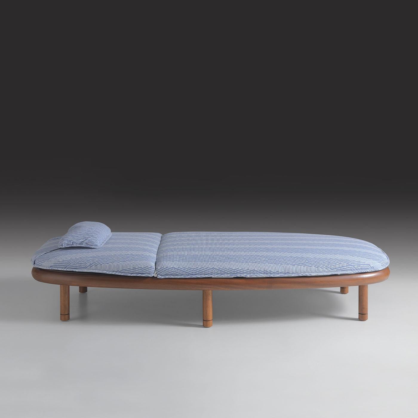 Defined by its elegant oval form and minimalistic Iroko wood frame, this outdoor lounger exudes refined simplicity. The light finish highlights the wood's natural grain, while an optional dark finish offers a dramatic contrast. Upholstered in PEI