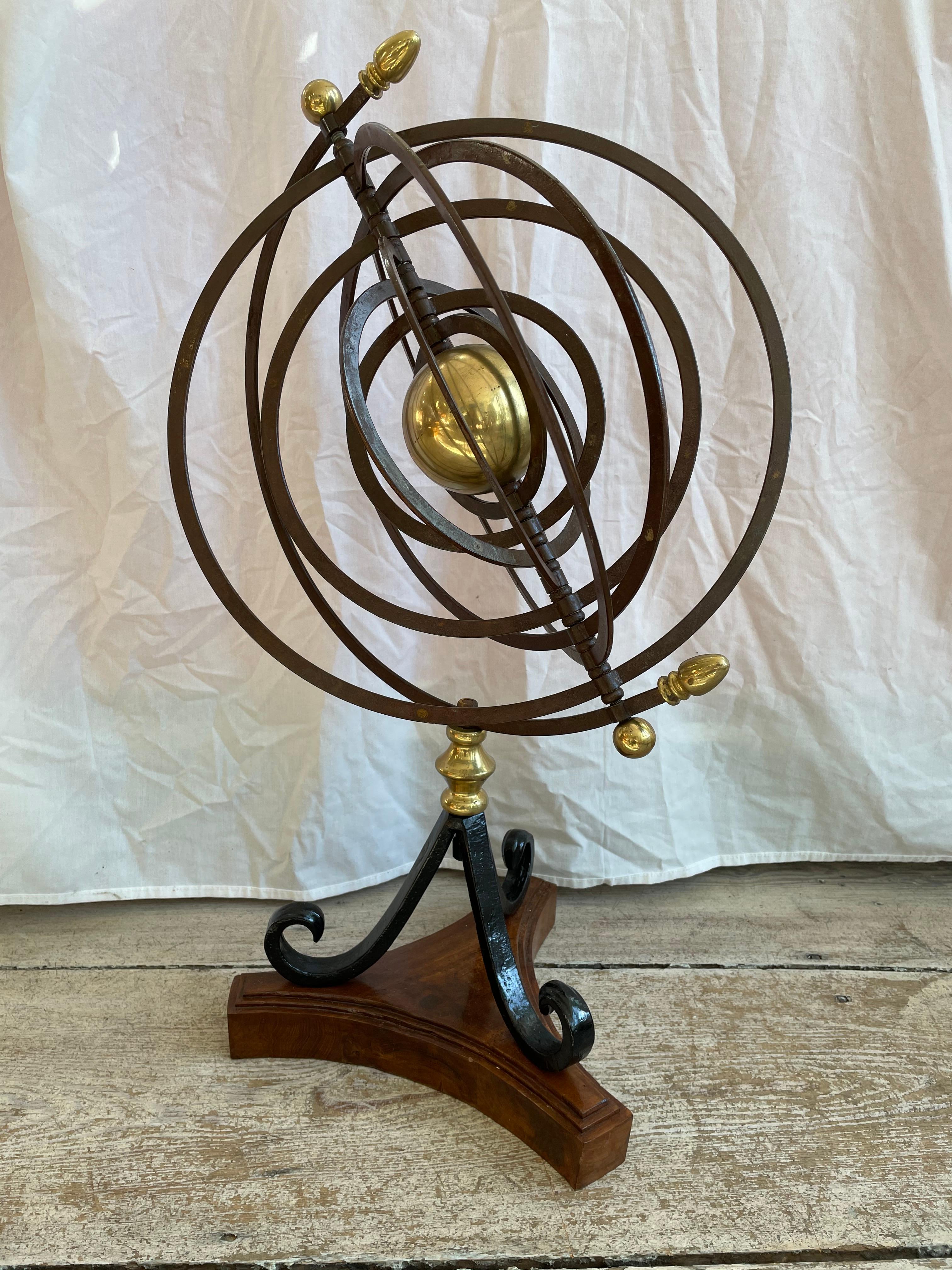An iron and brass celestial sphere Armillary on a teak base. Kinetic and dimensional with movable rings depicting the orbits of the 9 planets. The brass center represents the sun. The rings can also lay flat creating a totally different look. In two