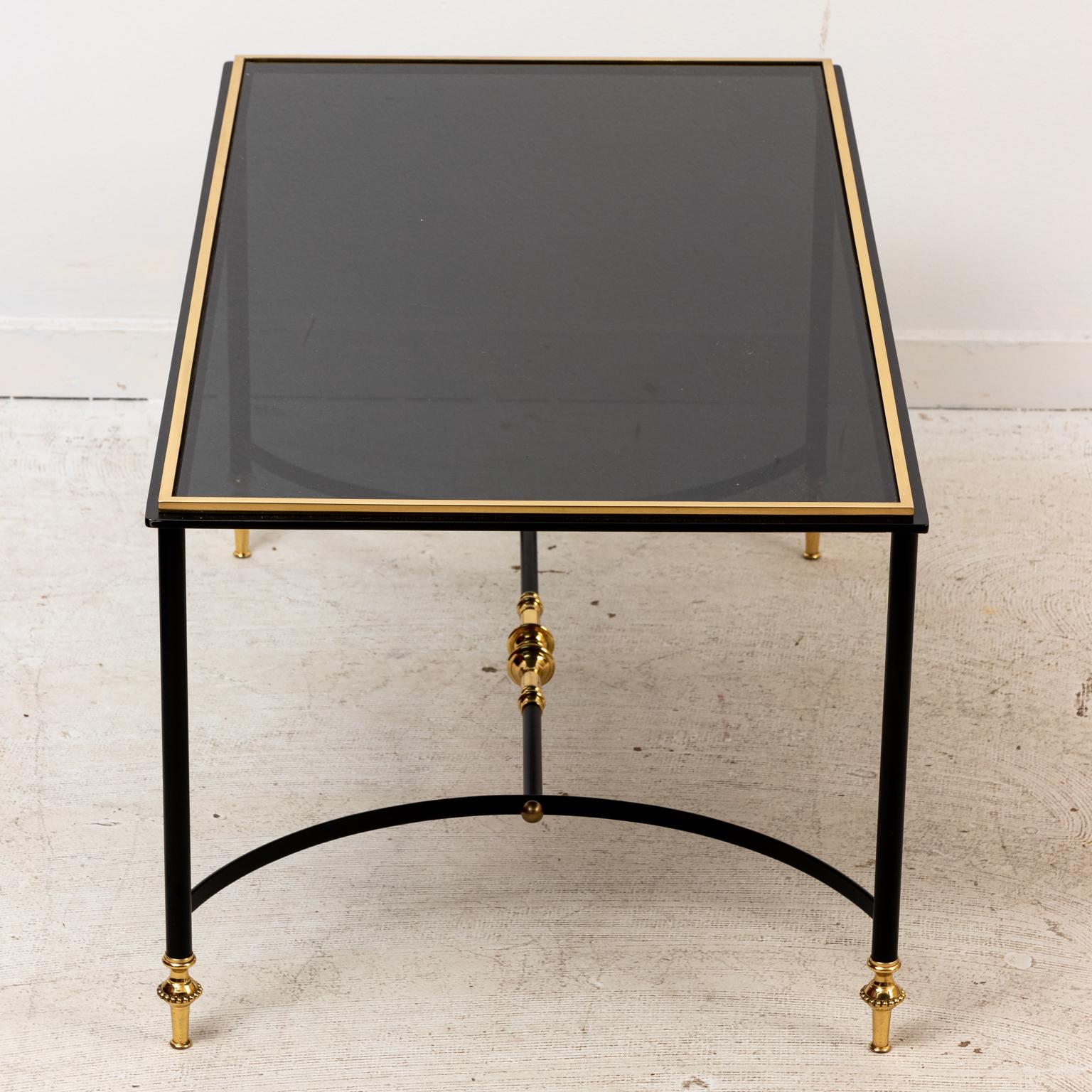 Iron and brass coffee table in the Hollywood Regency style with bottom cross stretcher. The piece is further detailed with polished brass trim and brass feet. Please note of wear consistent with age.