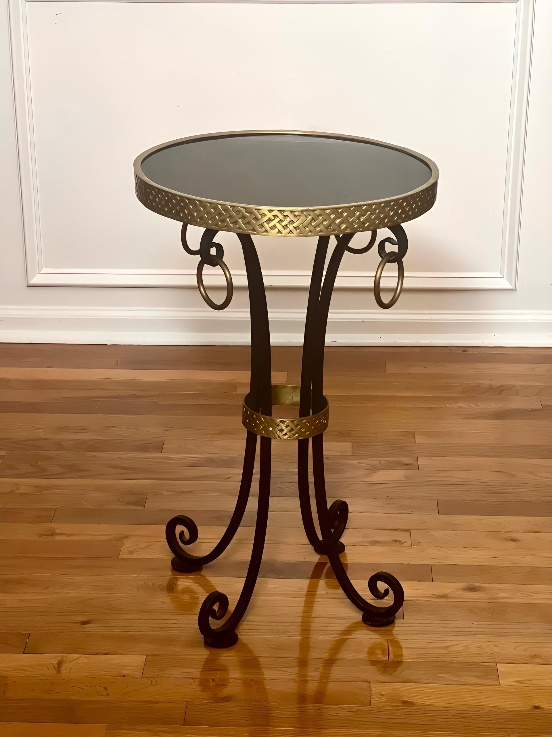 Guéridon en fer et laiton avec plateau en granit noir poli, fabriqué au milieu du 20e siècle. Magnifique table d'appoint dotée d'une lourde base en fer forgé avec quatre pieds galbés à double volute ornés de grands anneaux classiques en laiton