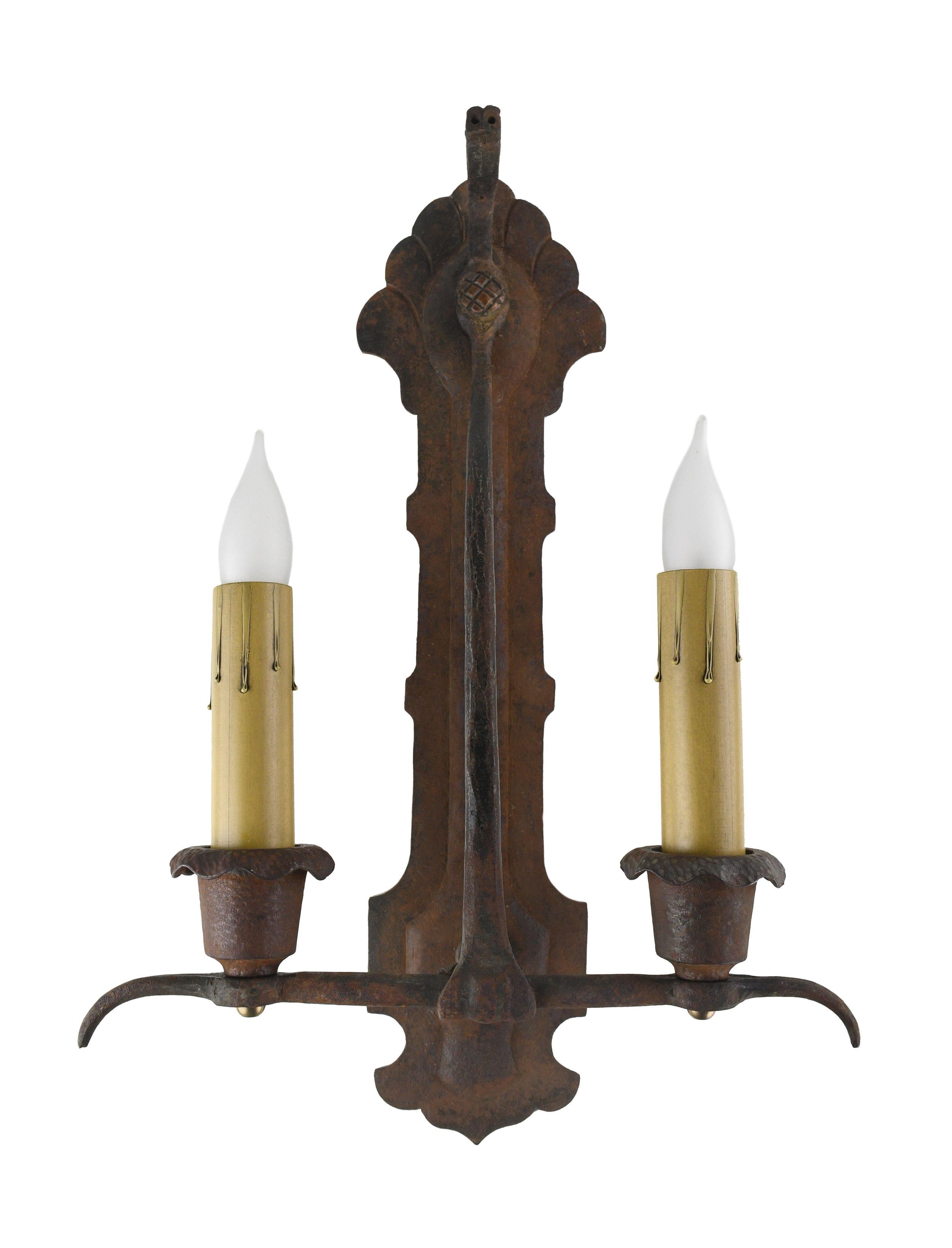 This stunning 2 candle sconce by Oscar Bach is alive with intricate details. A beautifully crafted dragon head centered by a scaly circular button rests at the top of the sconce. The geometric details in the design are pleasingly symmetrical. The