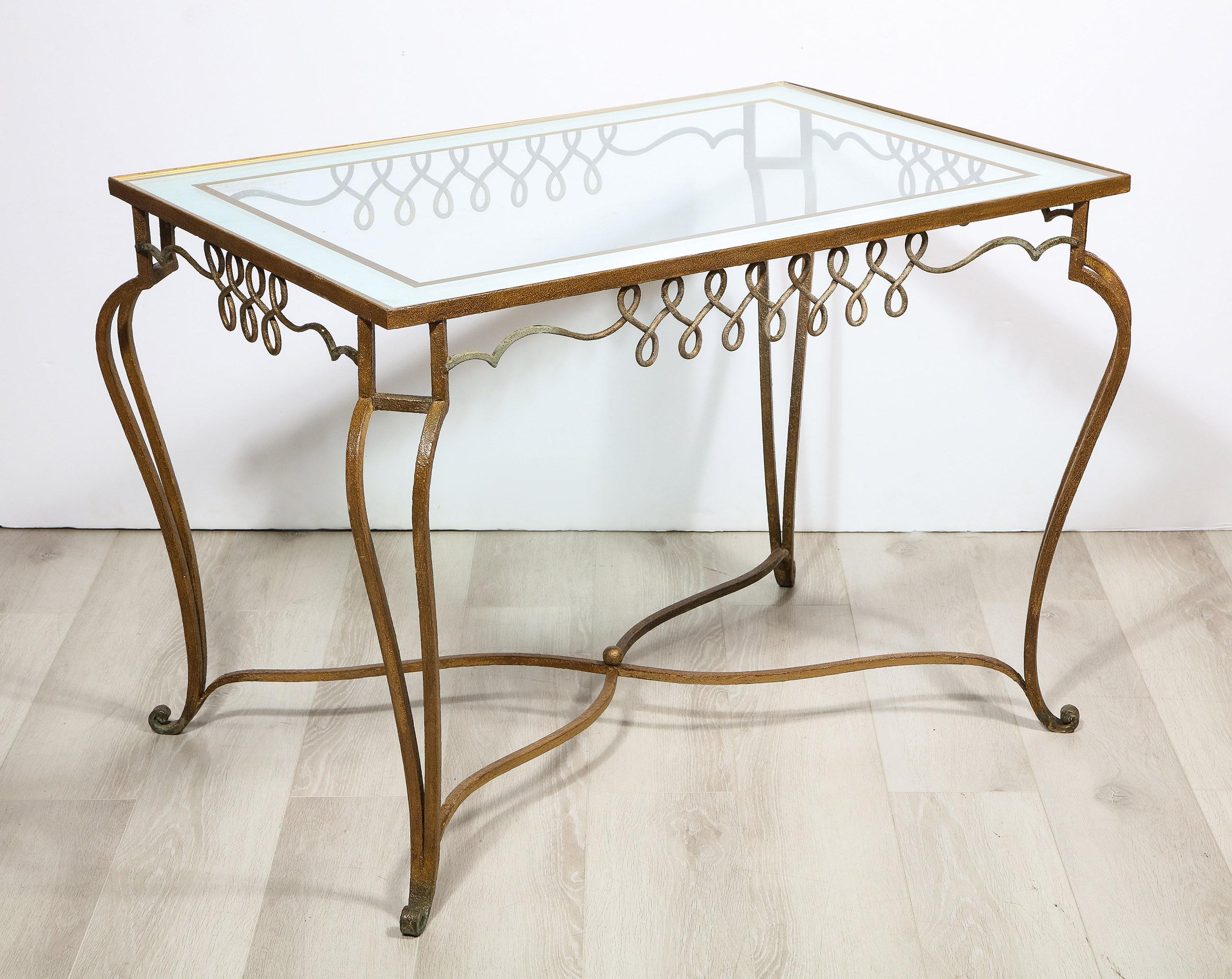 The Iron table attributed to René Prou, having an inserted glass top with framed in a mirrored and églomisé decoration supported by a finely embellished iron frieze with a scroll form legs at each corner and a central cross stretcher.