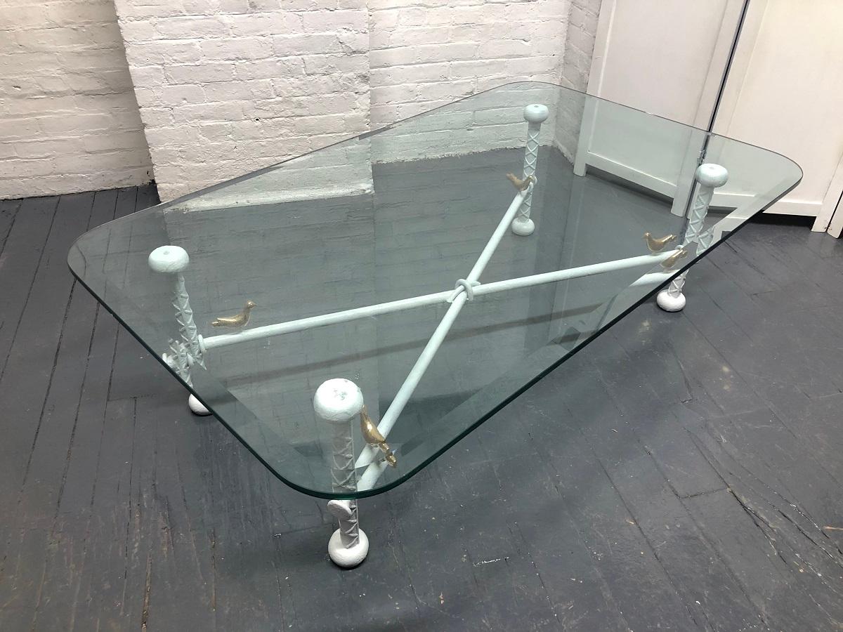 Iron and glass Brutalist coffee table style of Ilana Goor. The base is iron with a white lacquered finish with four painted gold birds. The table top has a thick beveled edge glass.