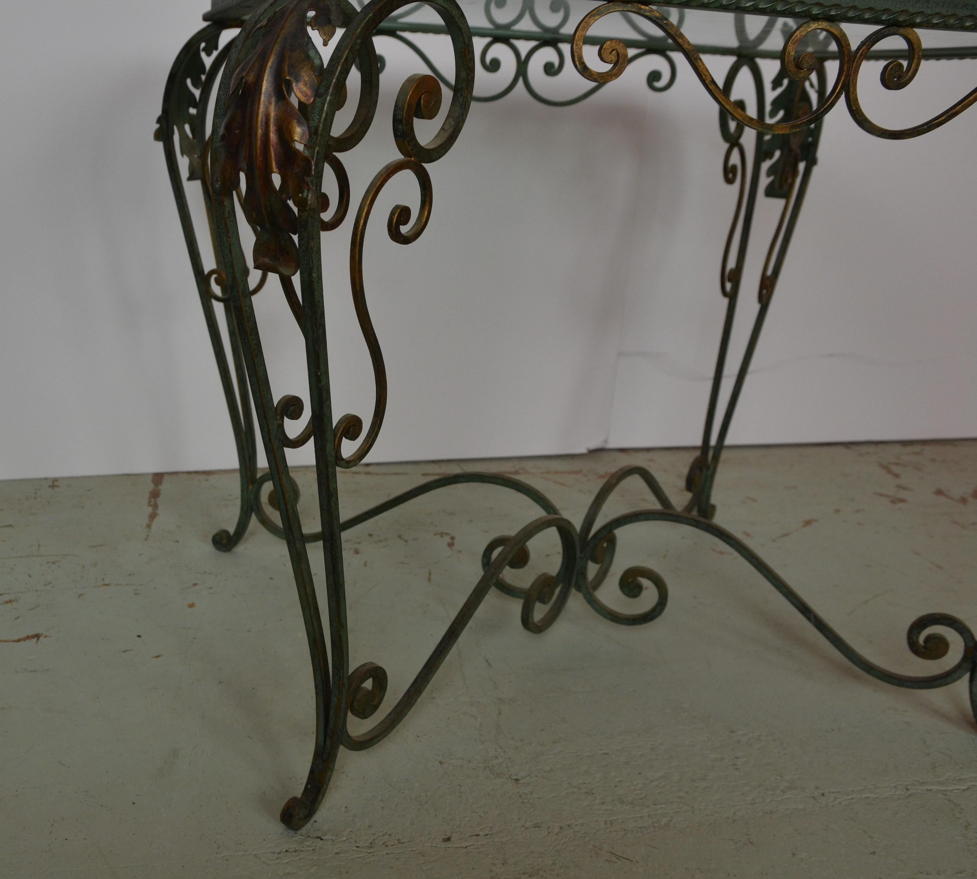 An iron end or coffee table with a green verdigris finish. Faded gilt / gold finish to the Acanthus leafs. Glass top.