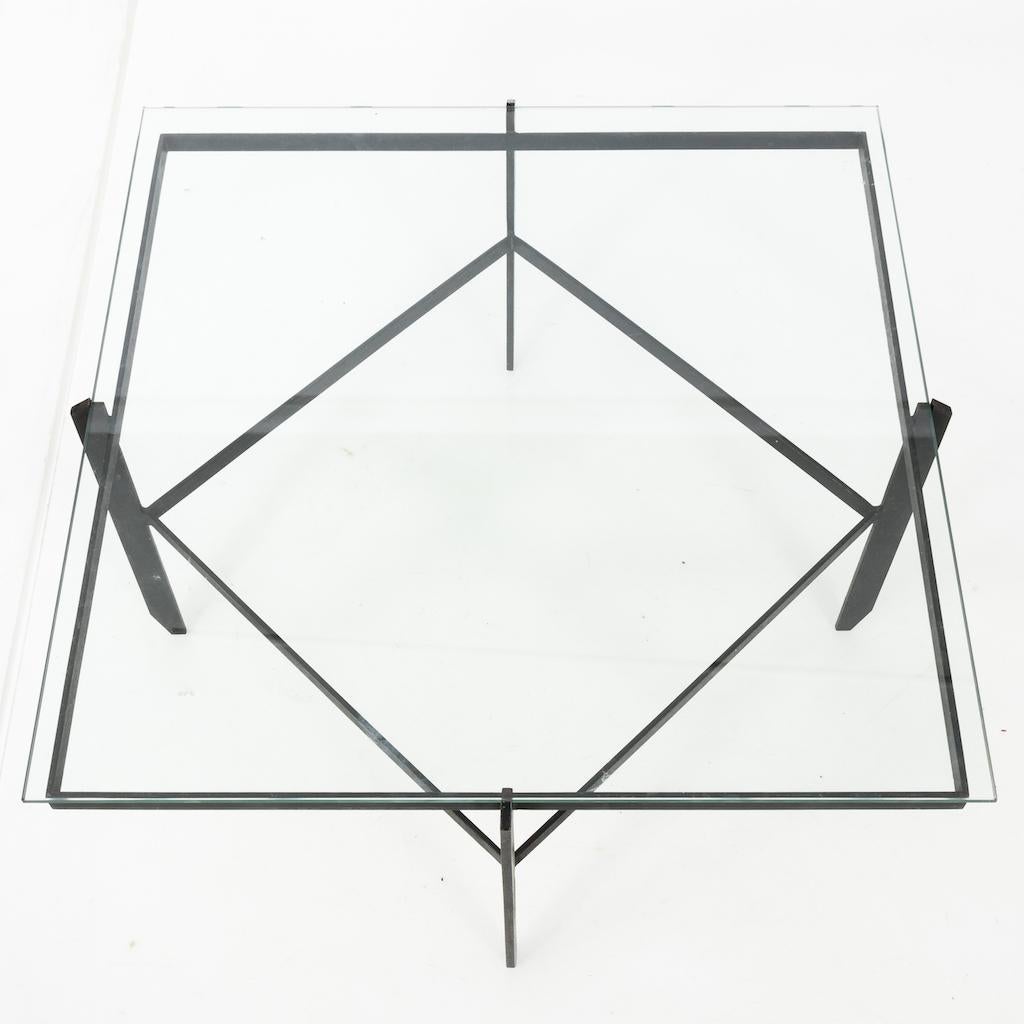 This Mid-Century cocktail table is a sleek and stylish piece that would elevate any living space. The table features a black iron base, giving it a modern and edgy look, while the glass top adds a touch of sophistication and elegance. The