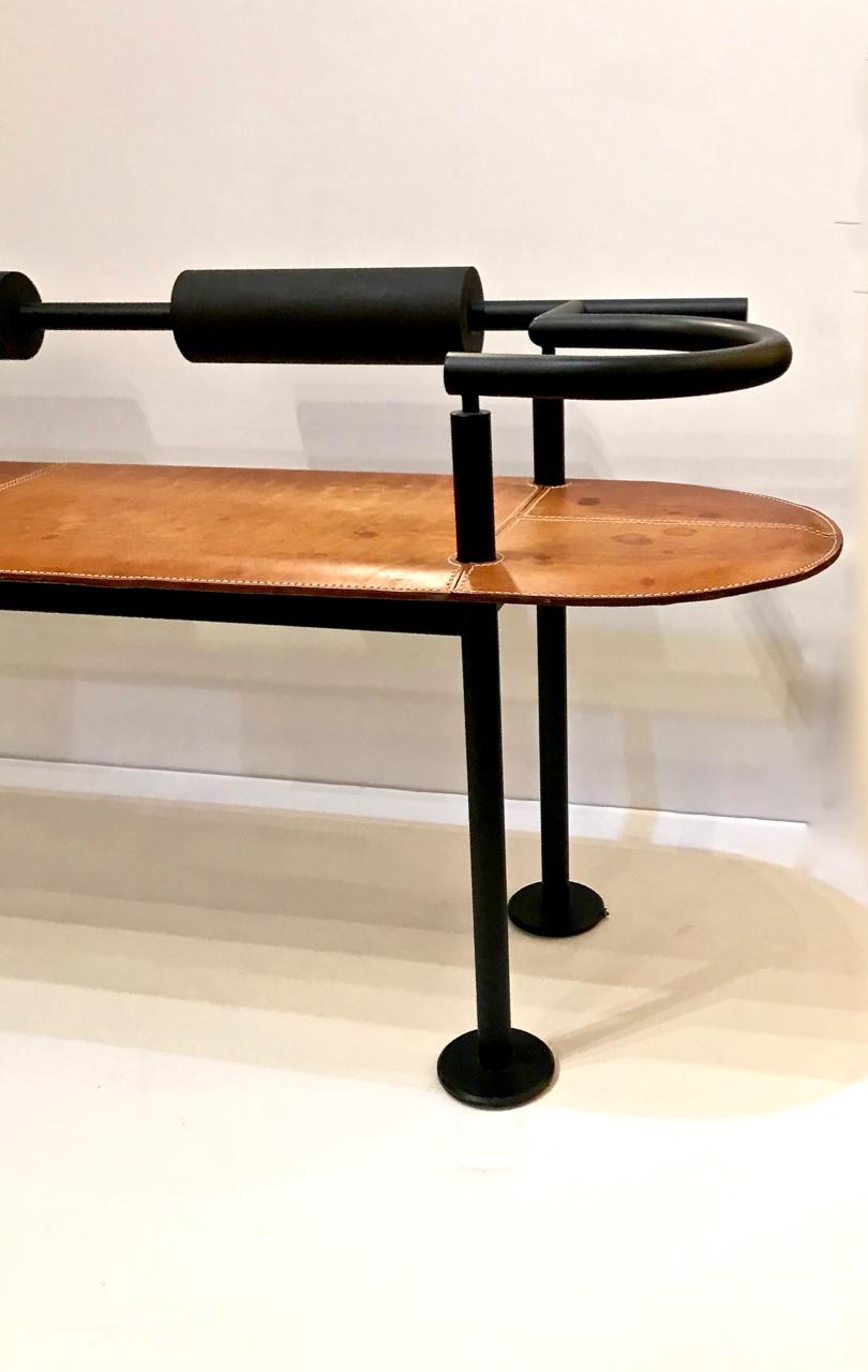 This is a striking midcentury iron and saddle leather bench detailed with hand stitching. The backrest is cushioned by two rolls of foam. The bench was designed by Cy Mann and was manufactured by Polflex in the 1980s. 