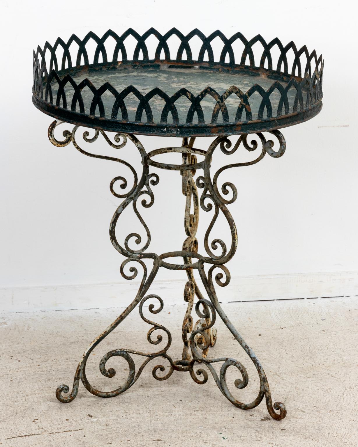 Iron and Tin plant table for garden or patio use on an s-scroll shaped pedestal base. The table is further accented with pointed arch gallery trim on the tabletop and remnants of original paint. Please note of wear consistent with age including
