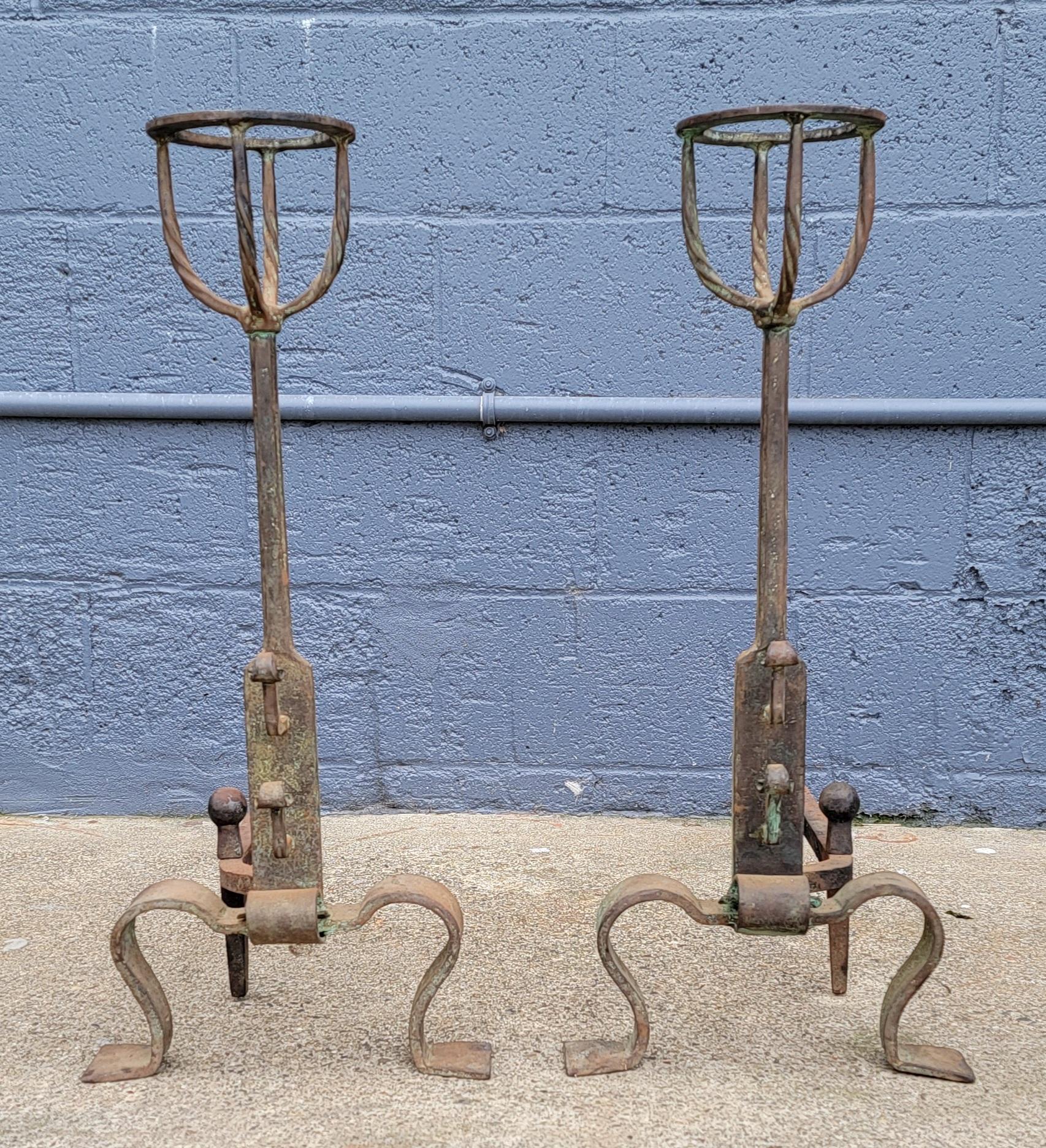 A pair of hand wrought iron andirons with basket tops. Includes iron poker. Hand hammering iron-smith marks evident showing the shaping, skill and workmanship of the maker. Basket tops were often used to warm bottles of brandy. Standing just over 26
