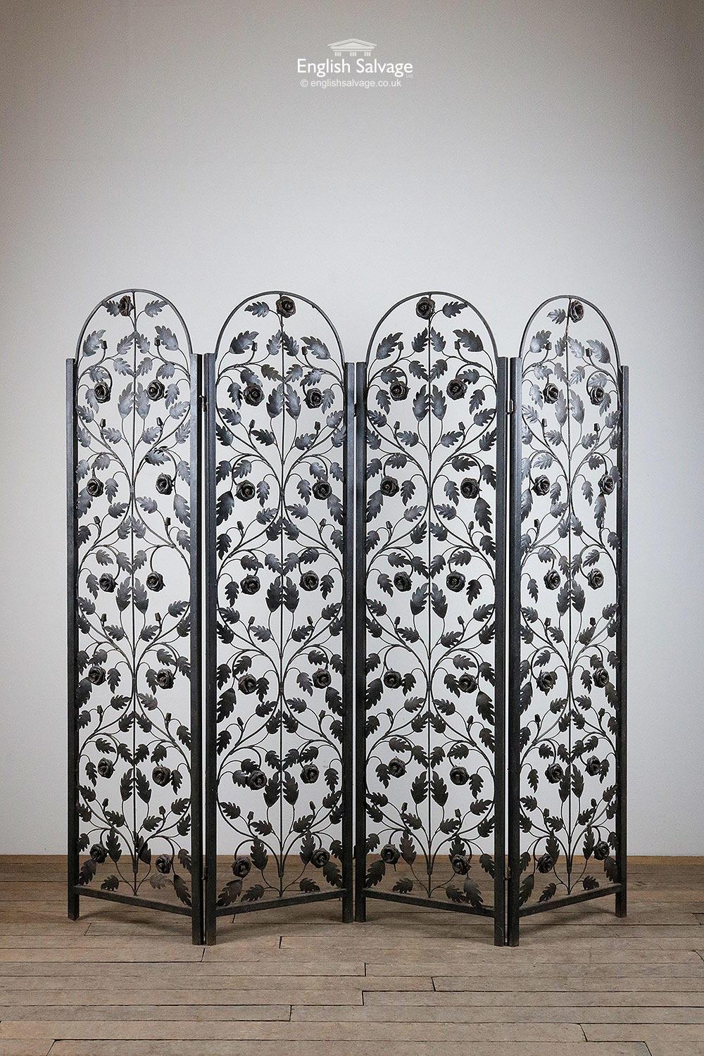 Ironwork four part folding screen / room divider with arched top detail. Pretty floral and foliate design throughout. Painted black, there is some surface rust and bends to the metal in places. The four sections (each measure 47.5cm wide) come