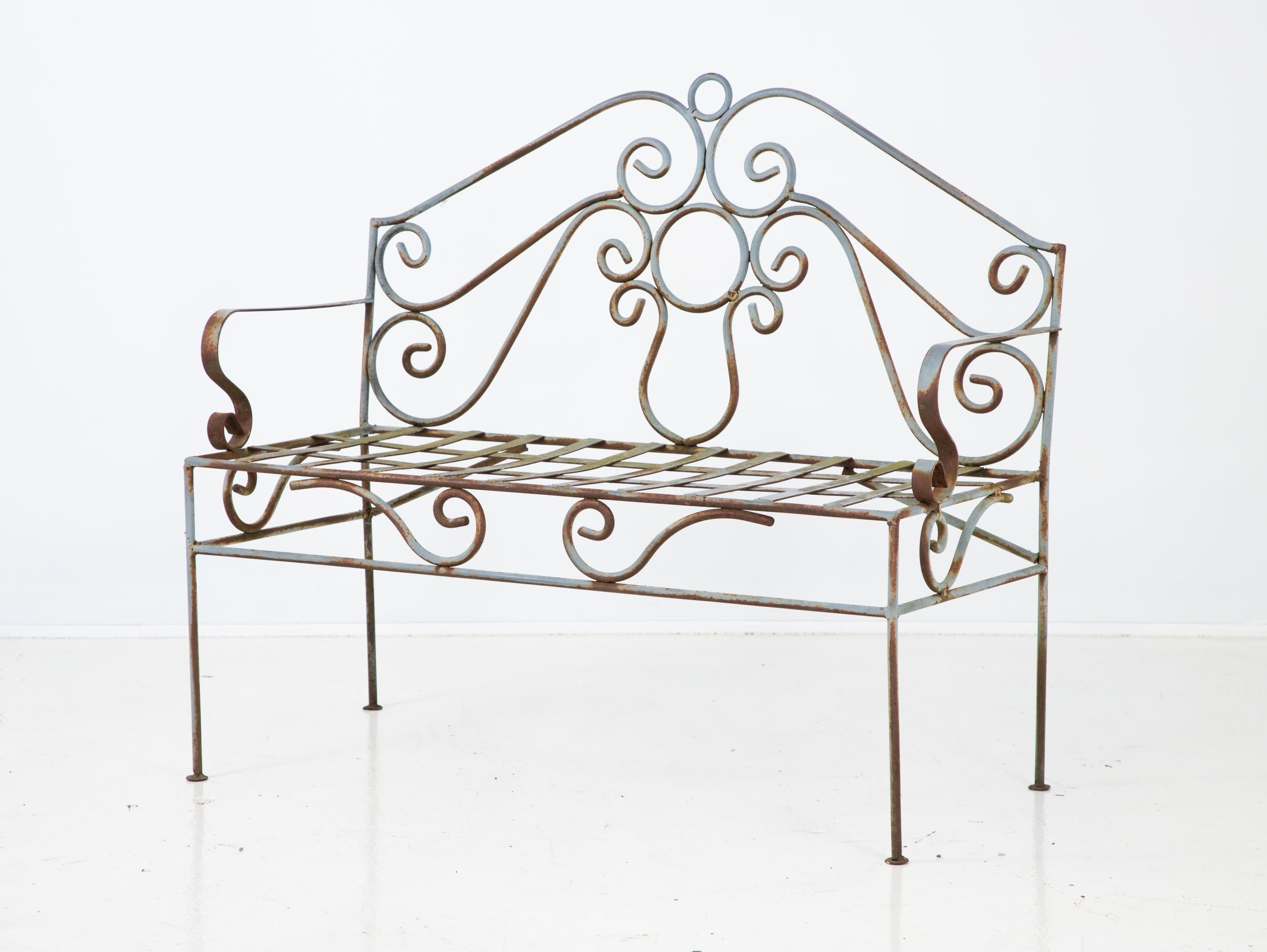 A French wrought iron bench with scroll back and arms. Repainted in slate blue color with some rust spots. Wear consistent with age and use. Seat height 16.5