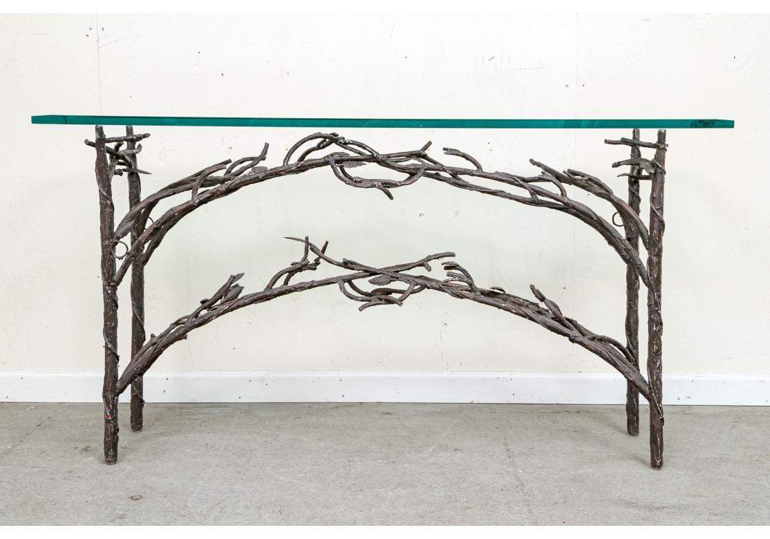 Table console en fer à branches bien travaillée, avec des branches feuillues entrelacées formant un double arc. Avec des ajouts de résine au cadre pour ajouter de la texture et le tout dans une patine profonde de type bronze. Plateau en verre