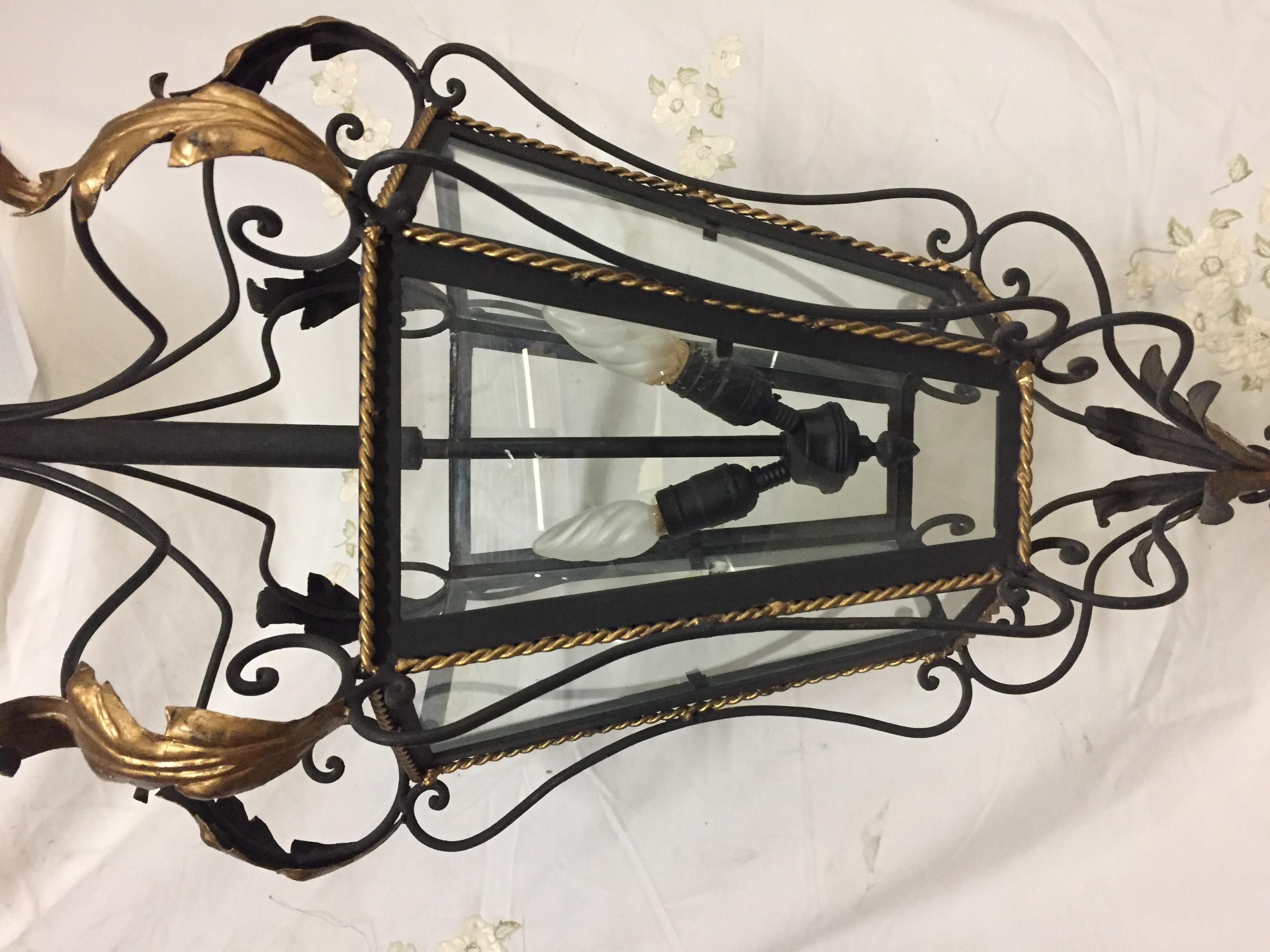 This grand chandelier makes a statement. The black painted iron frame has six glass tapered panels highlighted by gold painted twist and topped with flared gold painted leaves. There are 2 large base light sockets inside to provide high watt