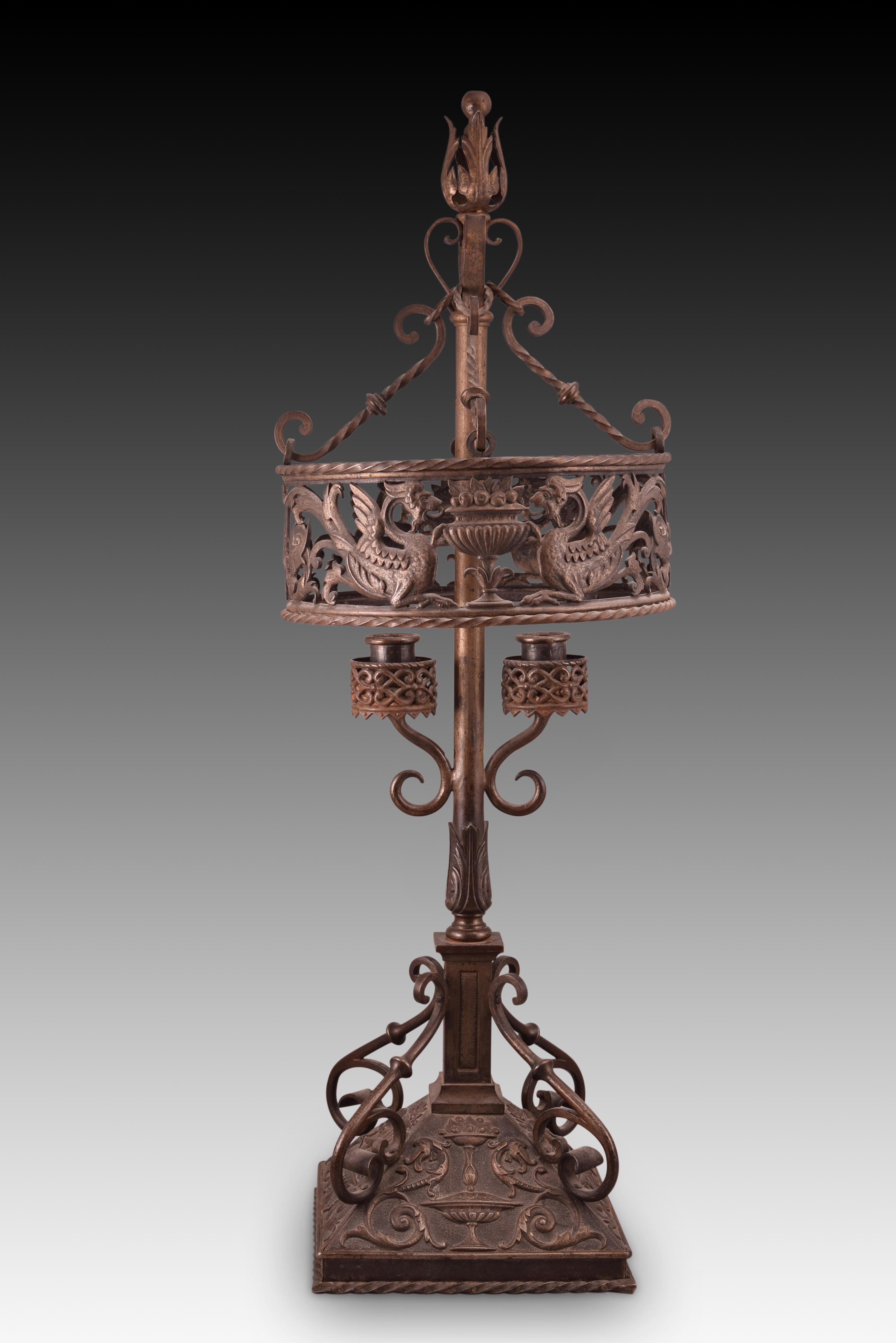 Neoplateresque lamp or candlestick. Wrought and embossed iron. Spain, towards the end of the 19th century. 
Two-light table chandelier made of wrought and embossed iron that has a square base, a balustraded axis with an architectural base and a