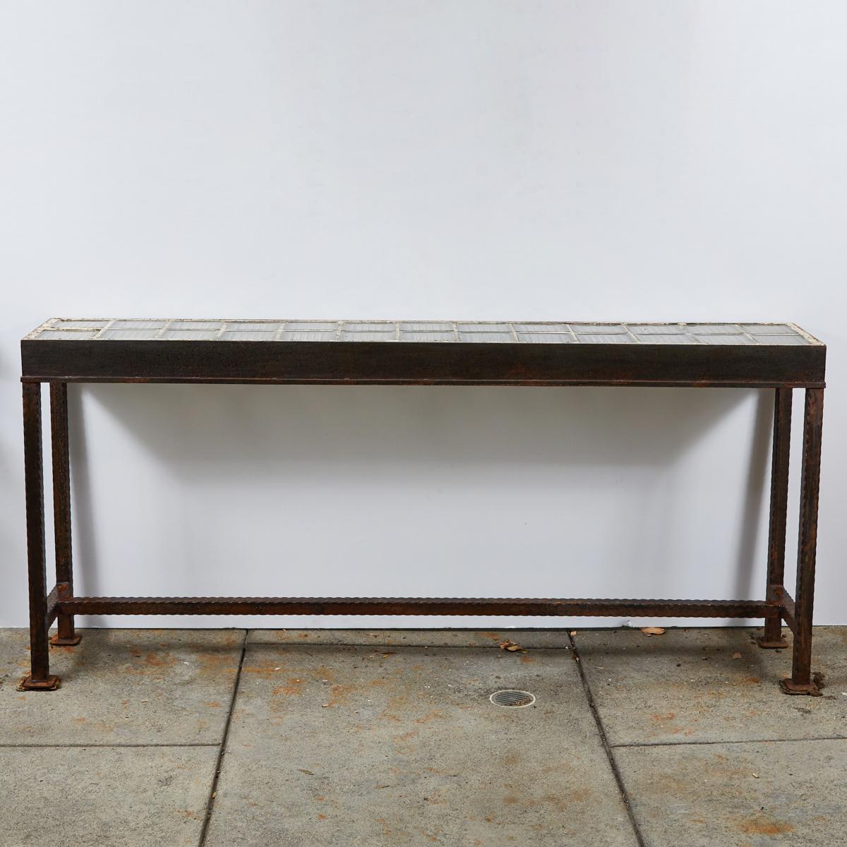 Mid-century iron console table with top made from vintage clear glass tiles. The tiles are square, lightly striated, and affixed in two rows with a cream-colored grout. The supportive iron framework has a smooth rectangular frieze and four straight,