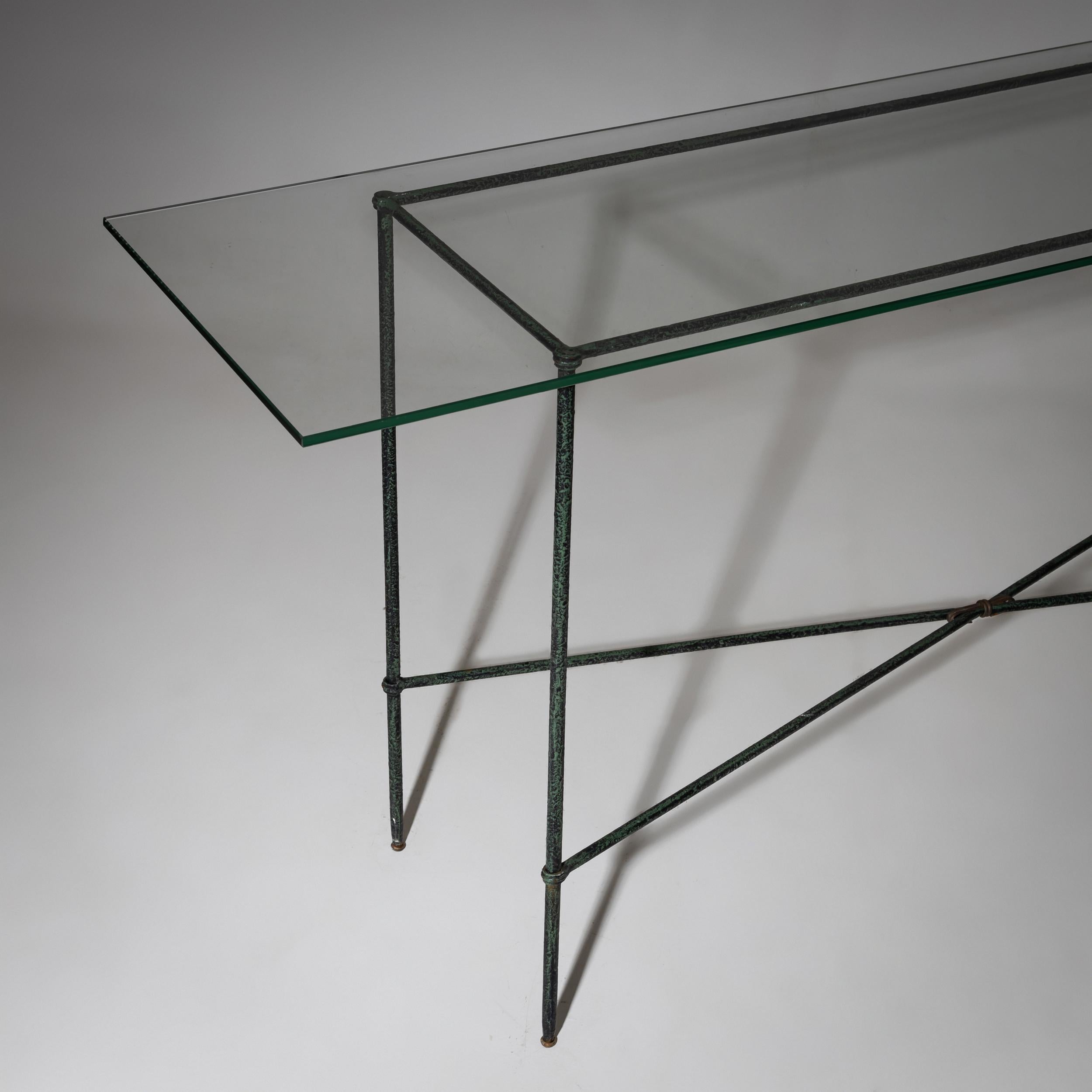 Narrow console table with a rectangular glass top and a green-patinated iron frame. The X-shaped crossbar provides stability and enhances the sleek, understated design.