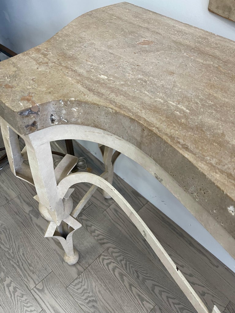 This console is finished in ivory with nice patina and some paint loss. The stone top is 2” thick . There are no chips on the top but around the edges it is consistently not filled in and shows natural inclusions in the stone. The base is iron.