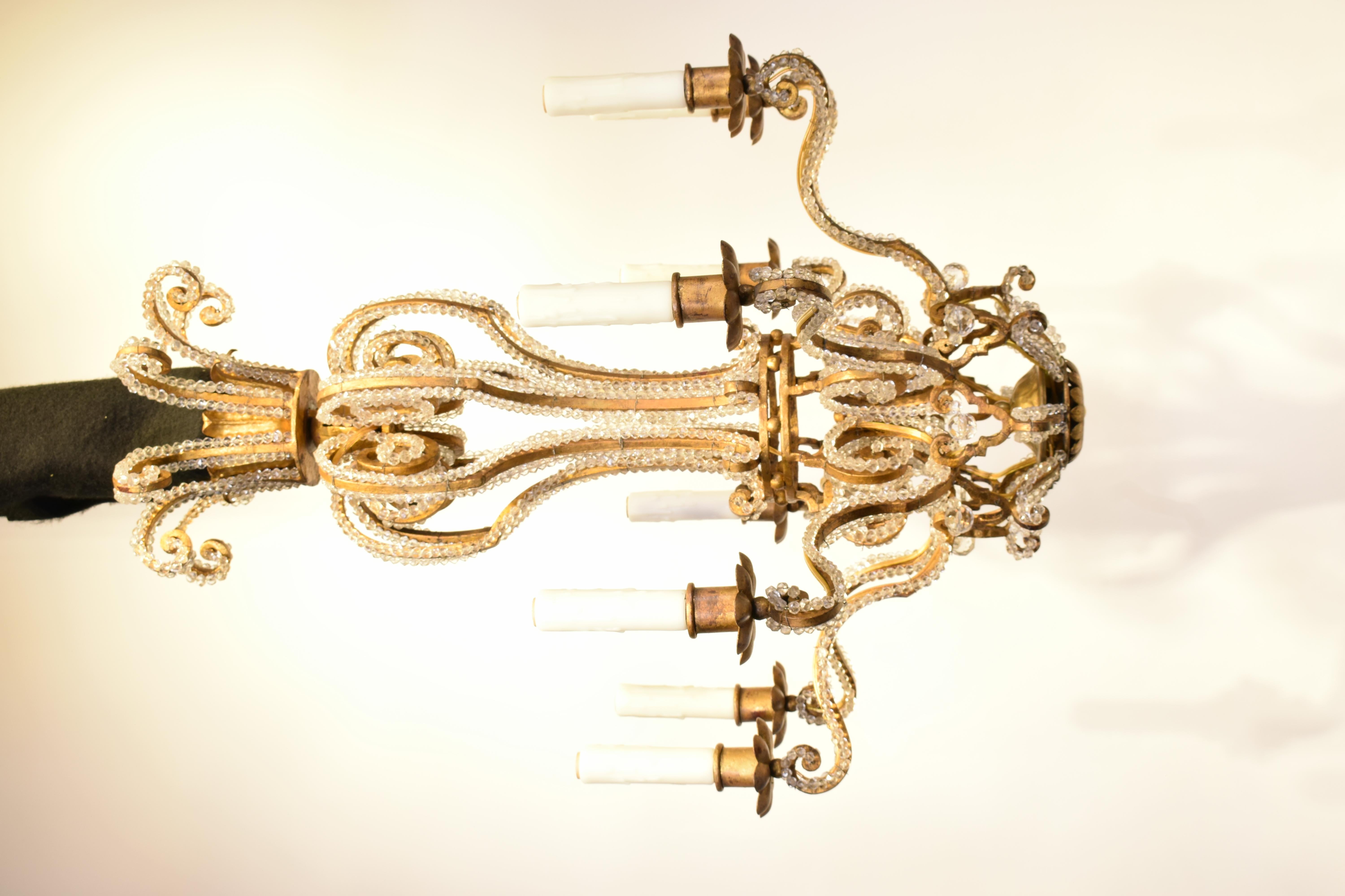 Ein feiner und eleganter Kronleuchter aus vergoldetem Eisen, verziert mit Ketten aus facettierten Perlen. 
Maison Jansen, Frankreich, um 1930. 8 Lichter.
Abmessungen: Höhe 29