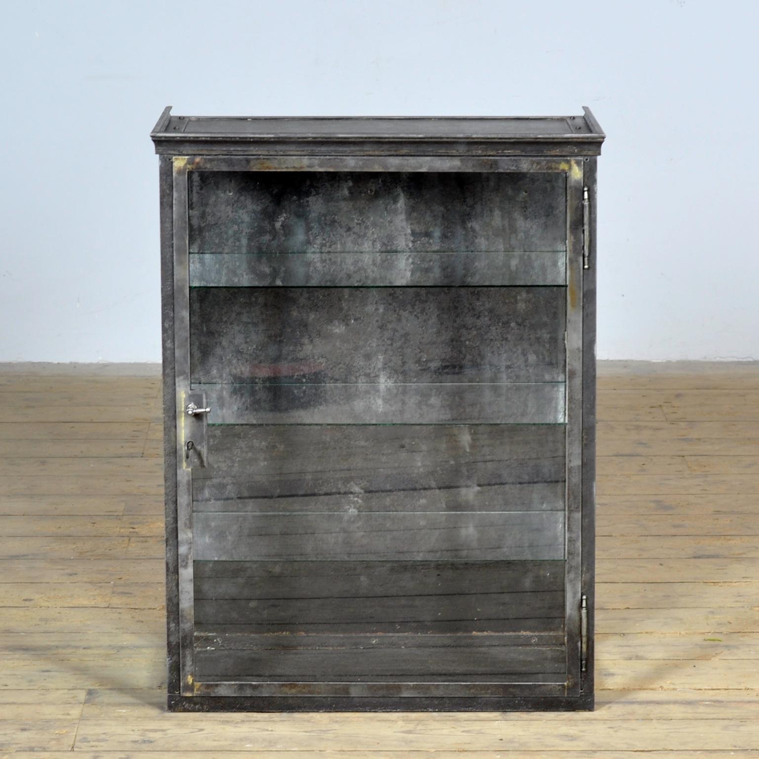 This polished iron display cabinet from the 1920s exudes pure industrial charm. With its sturdy metal frame and glass walls, it offers a stylish way to display your finest collections or curiosities. The cabinet has three glass shelves and a sturdy