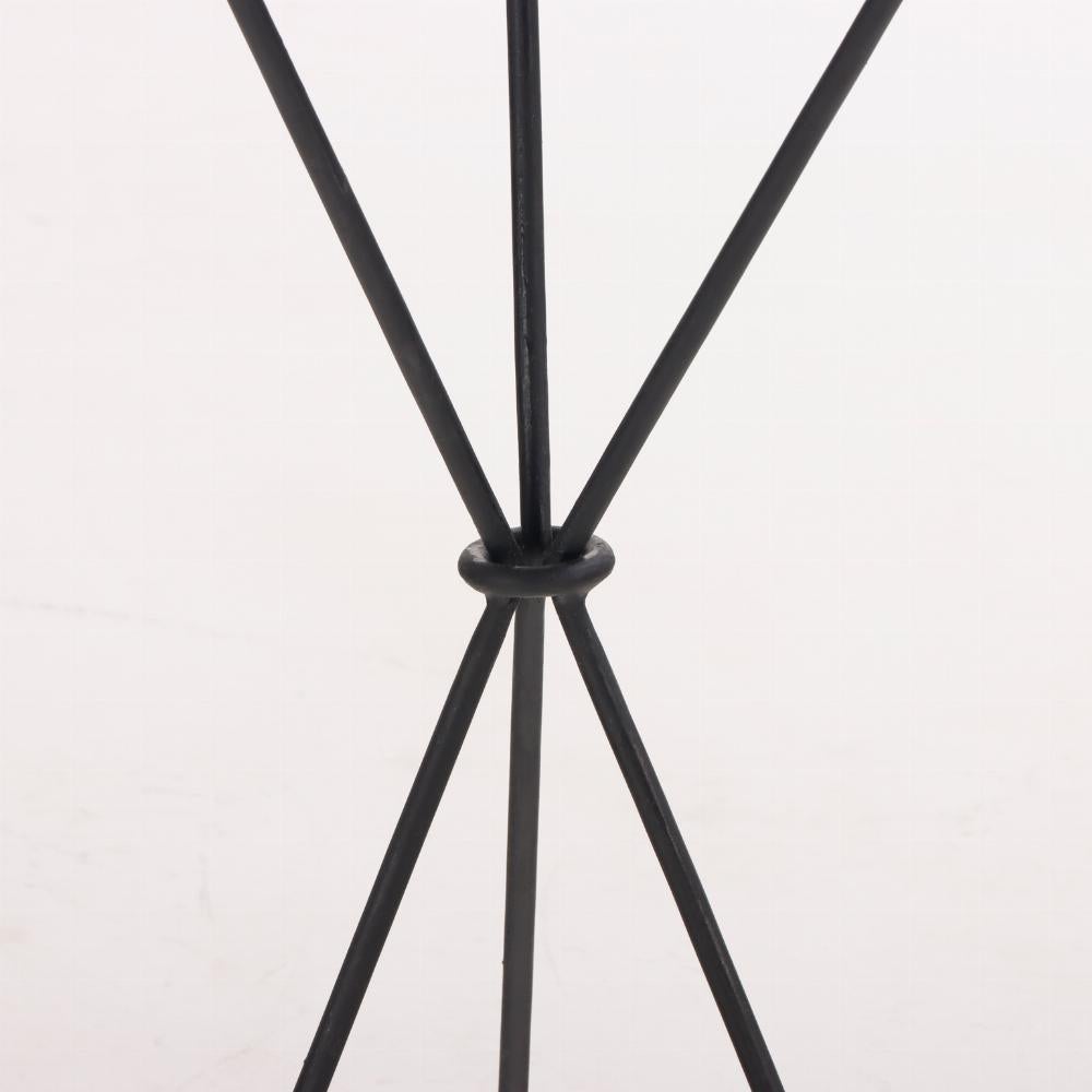 Un elegante tavolino in ferro alla maniera di Jean-Michel Frank con un piano rotondo rivestito di pergamena e un grembiule decorato con anelli di bronzo, sostenuto da una base tripartita in ferro.