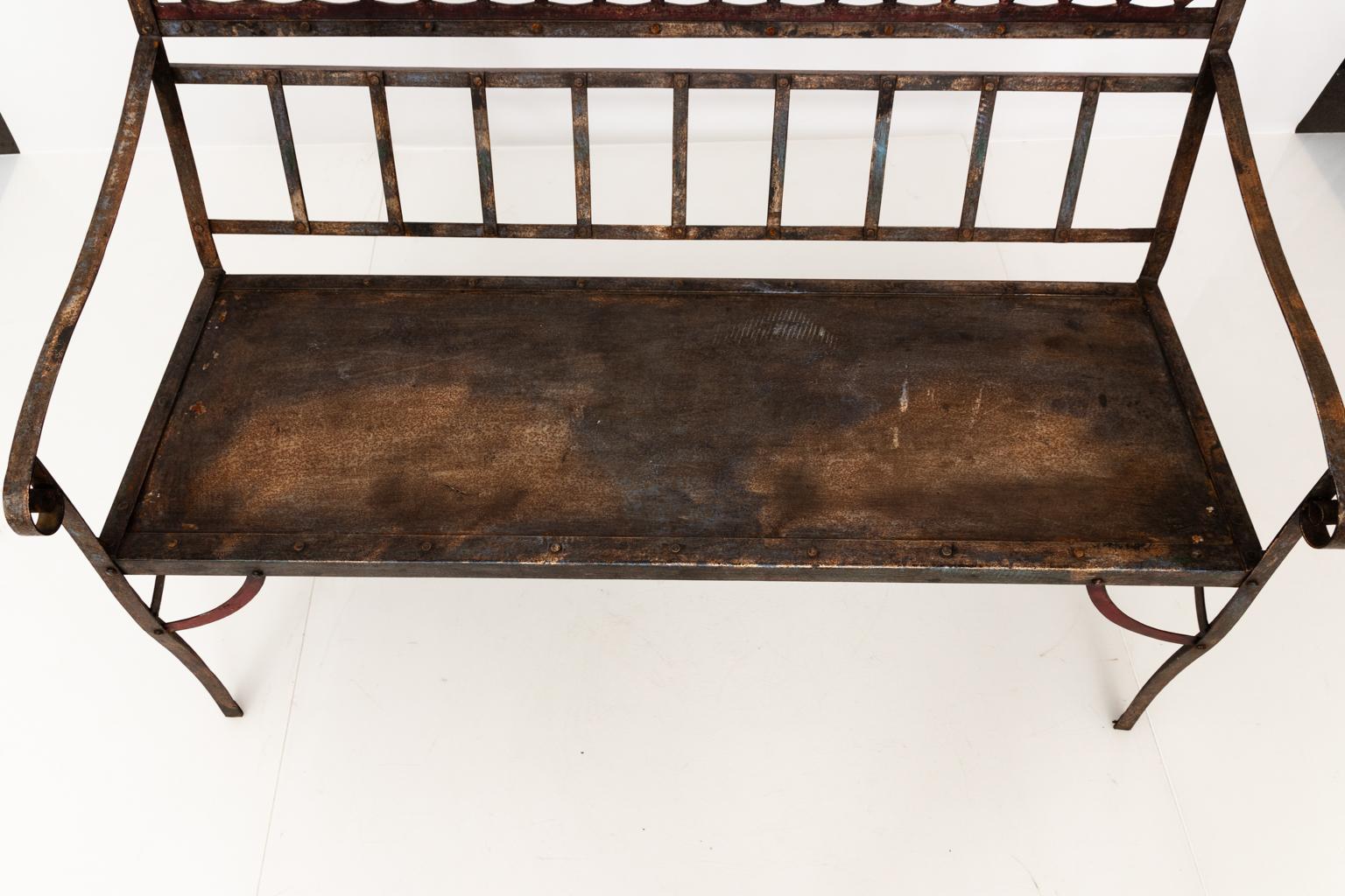 Iron garden bench with pierced back and scrolled arms, with traces of blue and red paint.
 