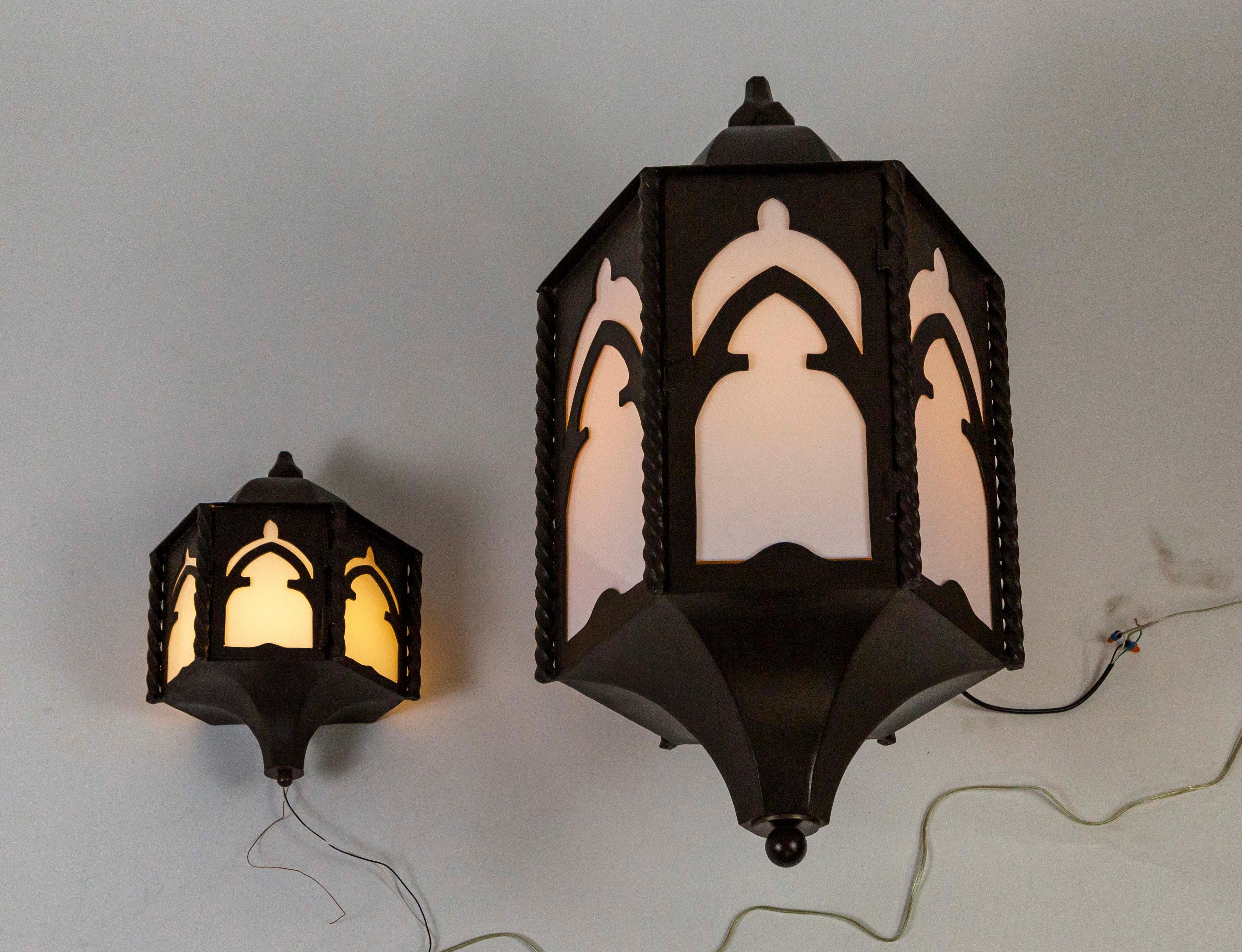 A pair of iron wall lanterns in a dome-capped, hexagon shape, with gothic arched panels and twisted column accents. They have newly installed, white glass plates and one medium base socket. Measures: 16.5