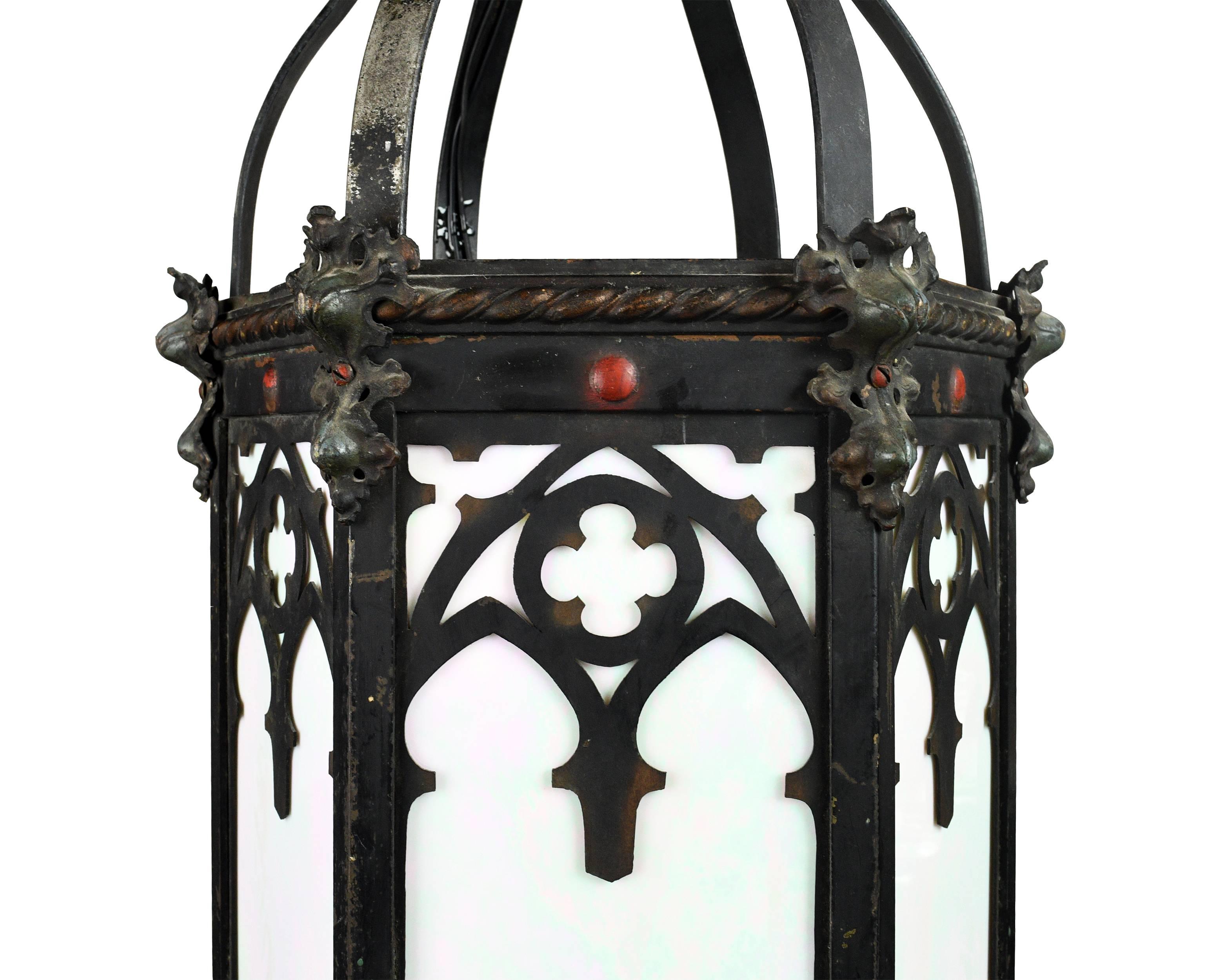 A majestic Gothic iron lantern light. The iron frame is heavy and solid with Gothic motifs on all sides of the fixture. Iridescent glass pieces are used for the shade, shimmering with pink and green hues when the light hits it just right. The heavy