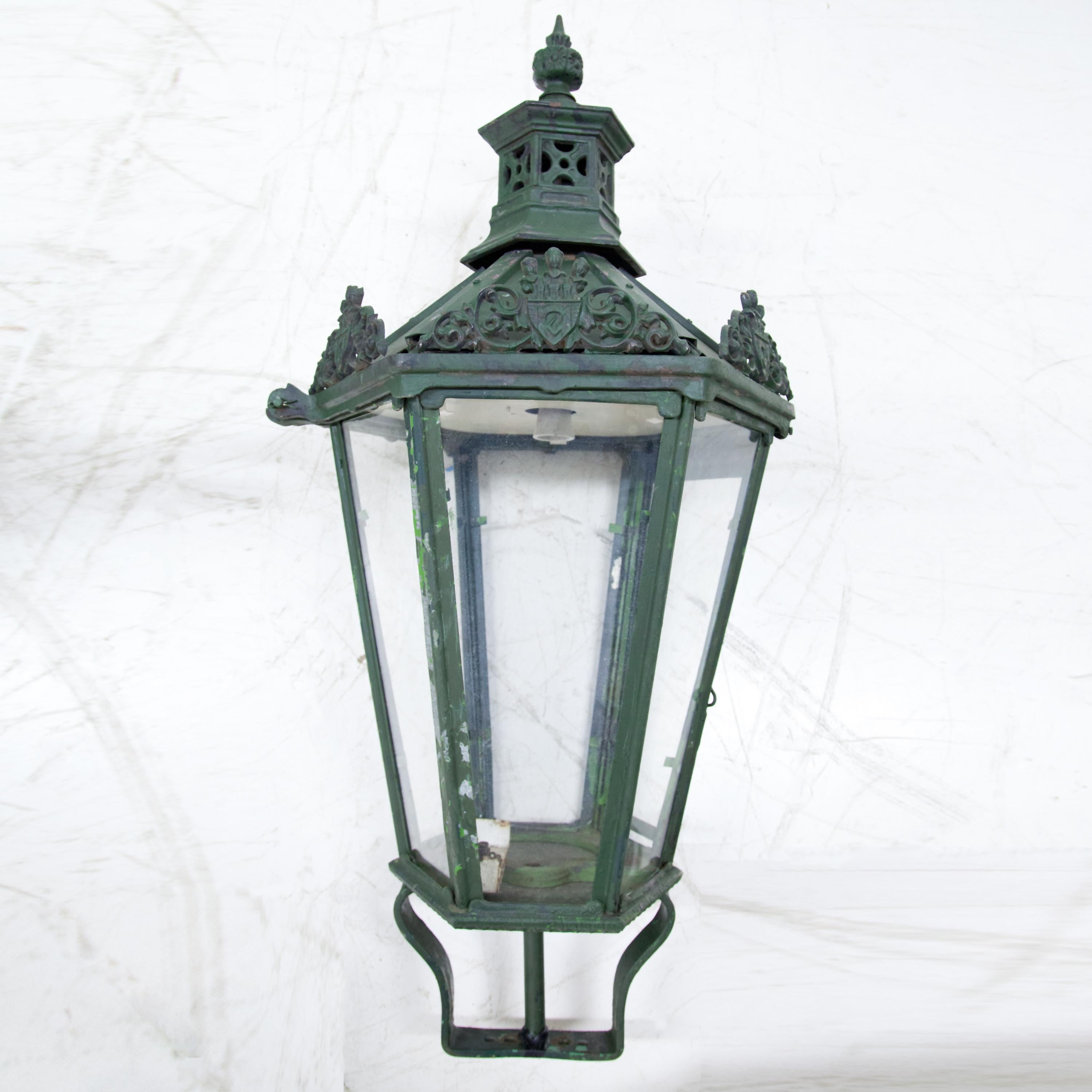 Pair of cast iron lanterns with hexagonal, glazed body and city coat of arms of Prague as decoration. Green patina.