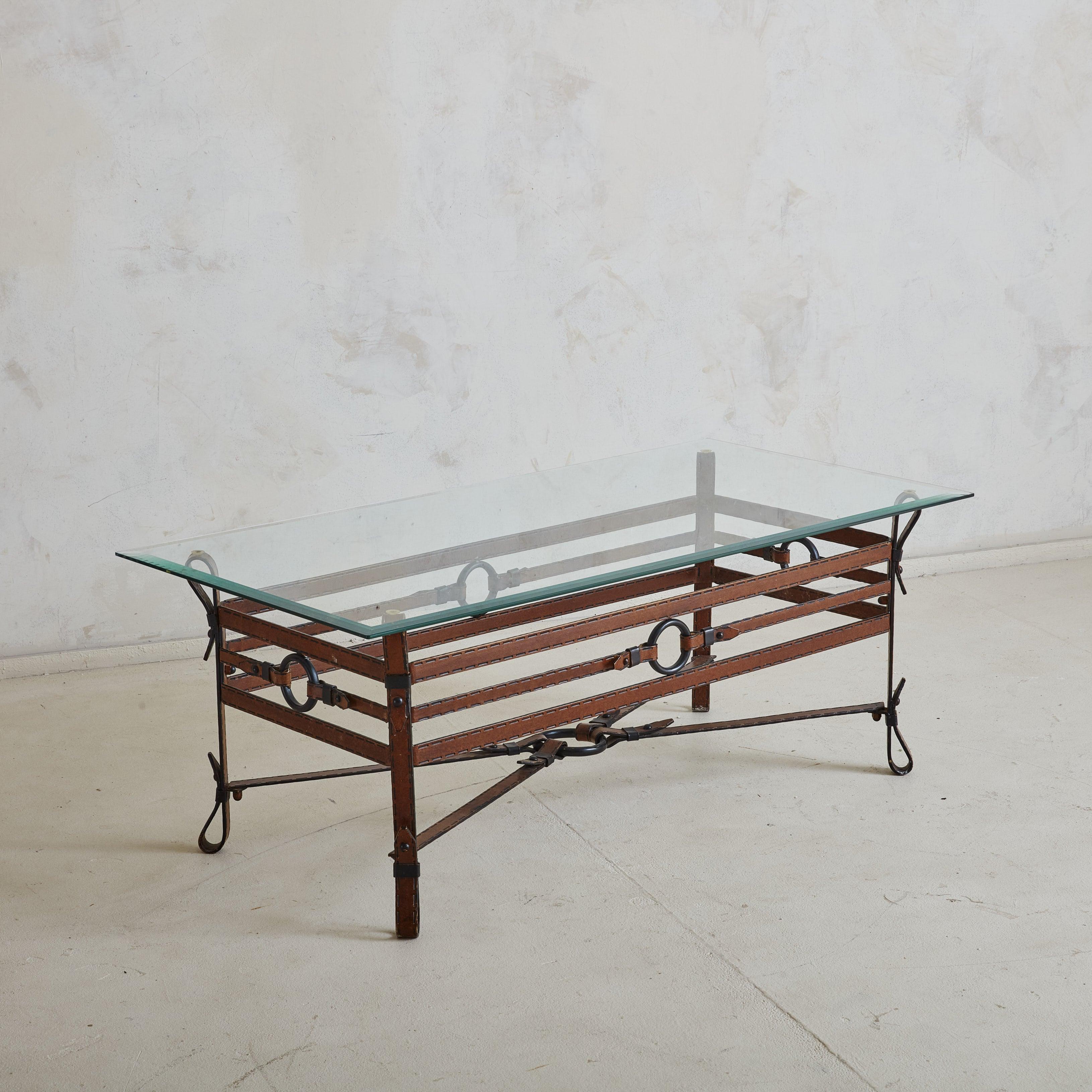 Une élégante table basse des années 1960 à la manière du designer et architecte français Jacques Adnet. La base de la table est composée de sangles en simili-cuir méticuleusement cousues, une caractéristique du style d'Adnet, qui sont habilement