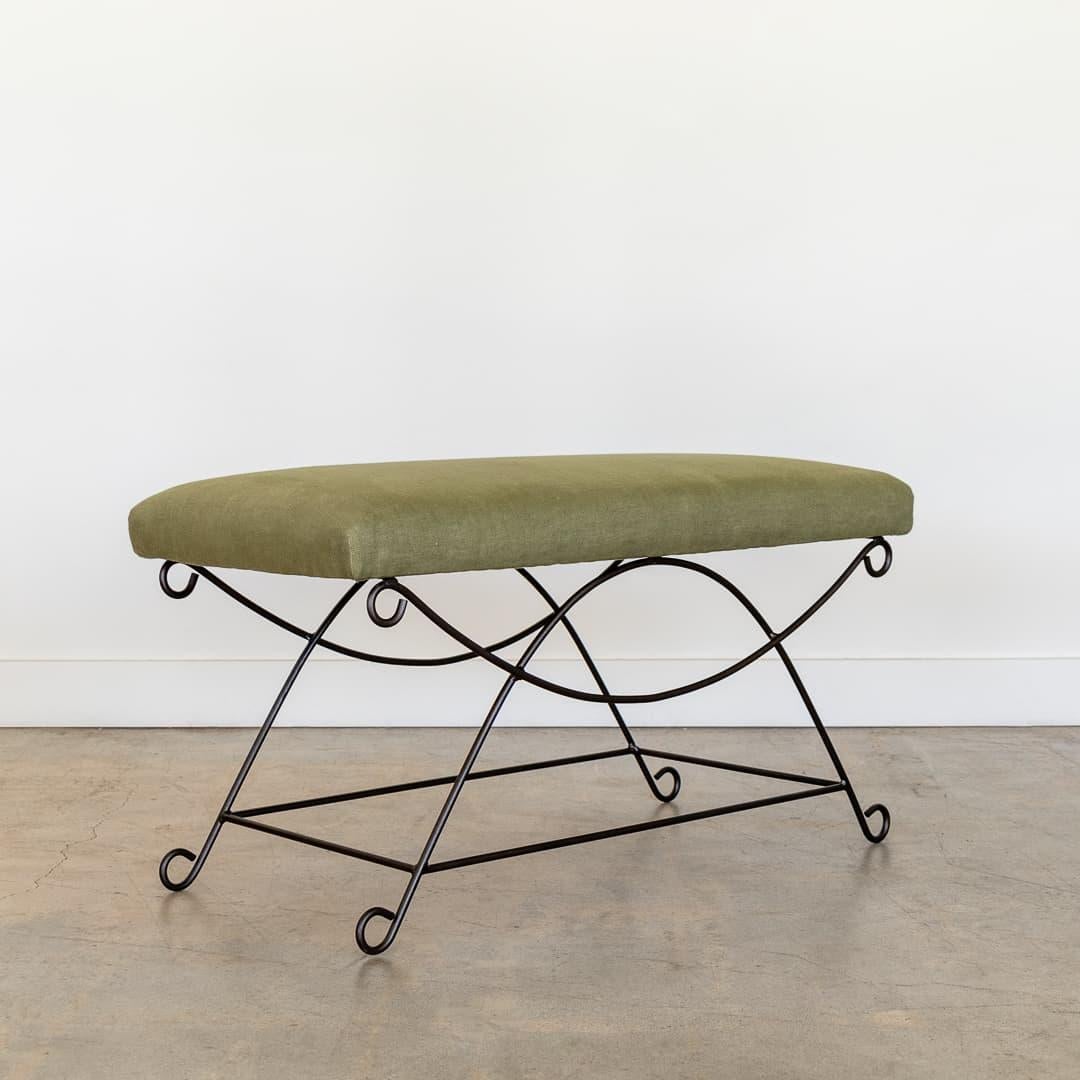 Beautiful iron bench with curved and looped base painted in a matte black finish. Rectangular cushioned seat upholstered in a green linen fabric or can be COM. Multiple available, sold individually.