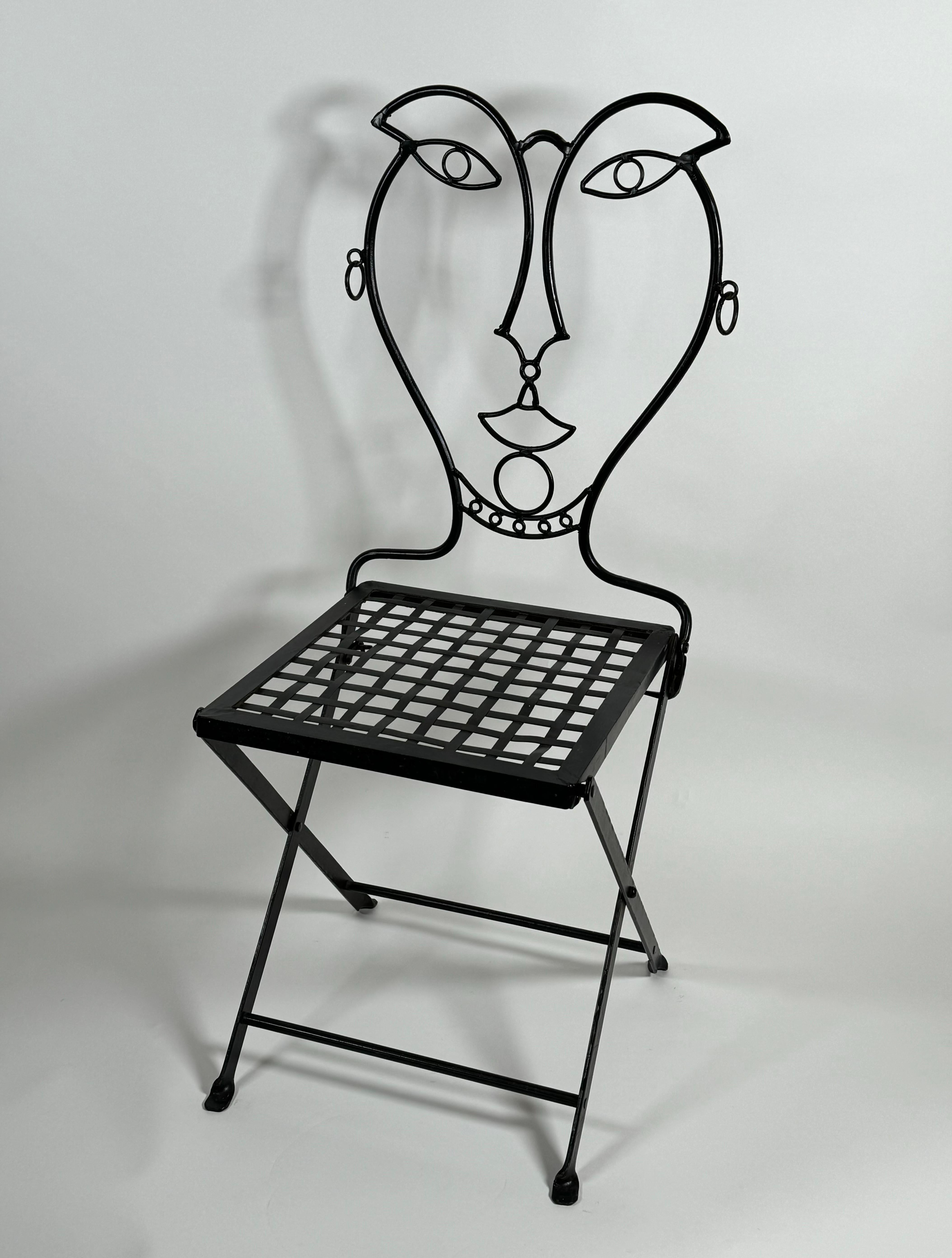 Folding handmade black painted iron chair from Mexico, the welded chair has a figurative abstract face for the seat back with loose earrings creating a whimsical chair for the patio in the garden or in a kitchen nook. The iron seat is an  lattice
