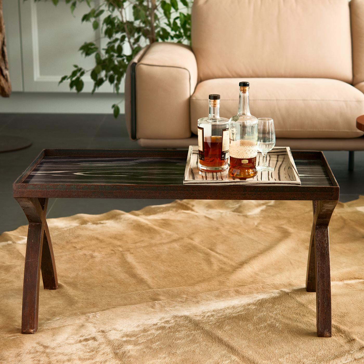 Exuding modern allure with its sleek and bold design, this coffee table is characterized by a dynamic interplay of materials and geometric shapes. The rectangular top is raised on two curved, criss-crossed legs in dark wood-veneer on each side, and
